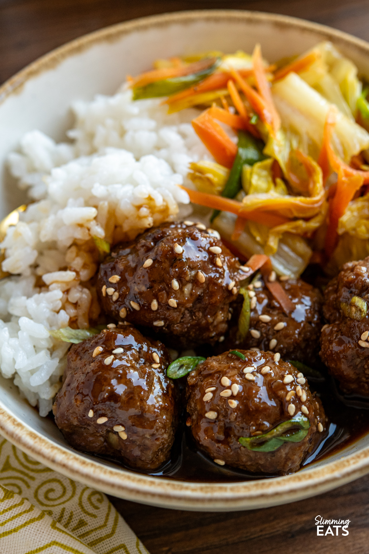 close up of serving of Teriyaki Meatballs in a beige rimmed white bowl with stir fry veg and rice