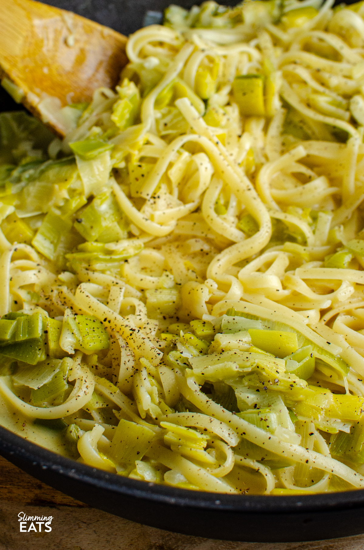 close up of One Pot Creamy Cheesy Leek Pasta in non stick skillet with wooden spoon 