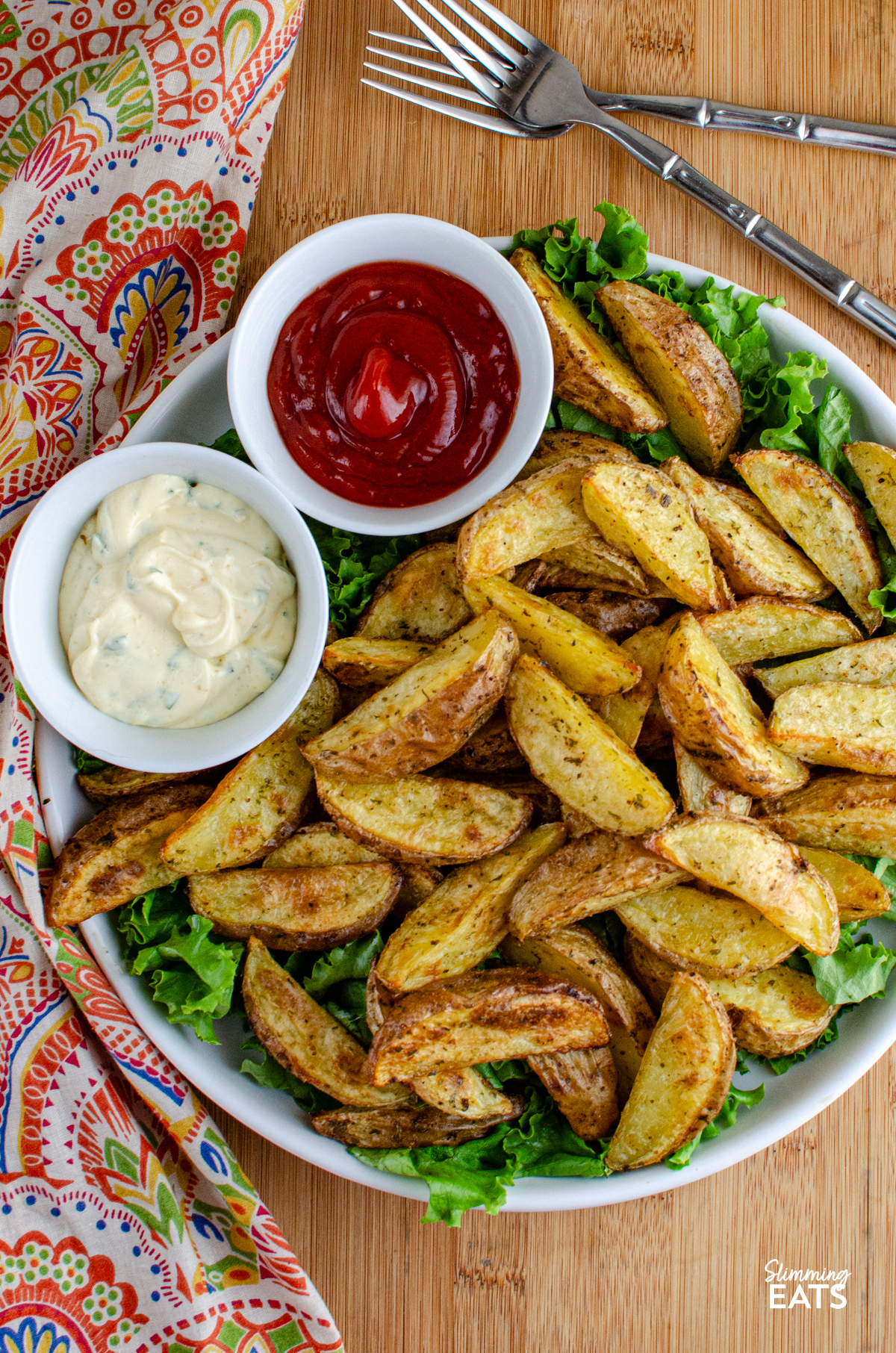 Tuck into these tasty Garlic and Herb Potato Wedges, a perfect side dish to round out just about any meal, and without the guilt too. Crispy on the outside, fluffy in the middle, they're everything you want from a good wedge and so easy to make at home. Garlic and Herb Potato Wedges in a bowl with lettuce, ketchup and garlic mayo.