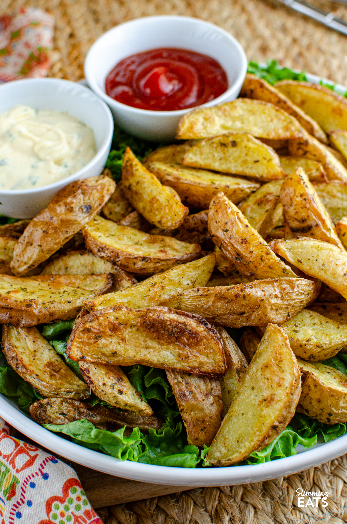 Tuck into these tasty Garlic and Herb Potato Wedges, a perfect side dish to round out just about any meal, and without the guilt too. Crispy on the outside, fluffy in the middle, they’re everything you want from a good wedge and so easy to make at home. Garlic and Herb Potato Wedges in a bowl with lettuce, ketchup and garlic mayo.