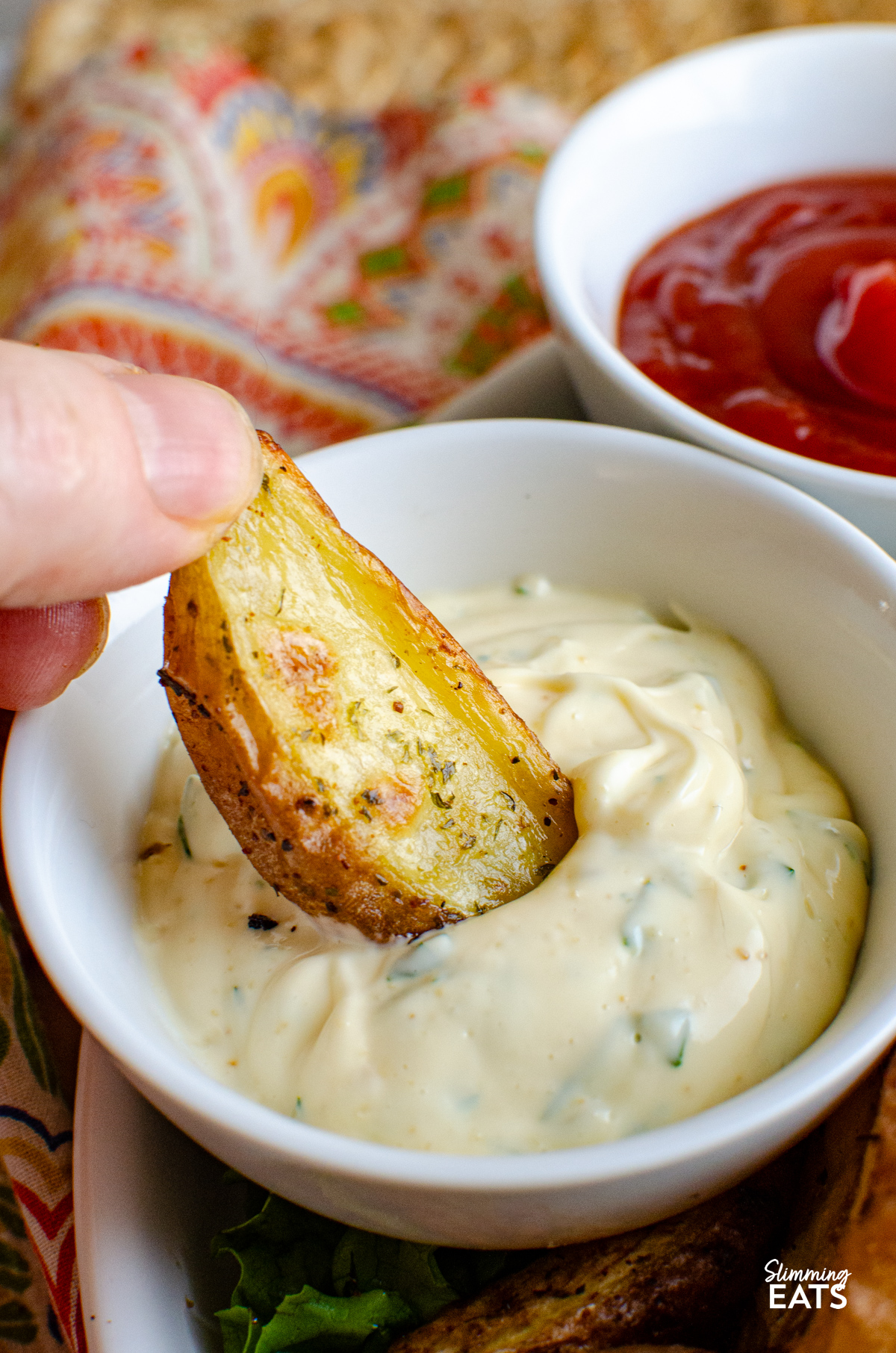 Tuck into these tasty Garlic and Herb Potato Wedges, a perfect side dish to round out just about any meal, and without the guilt too. Crispy on the outside, fluffy in the middle, they’re everything you want from a good wedge and so easy to make at home. garlic herb potato wedges being dunked into garlic mayo