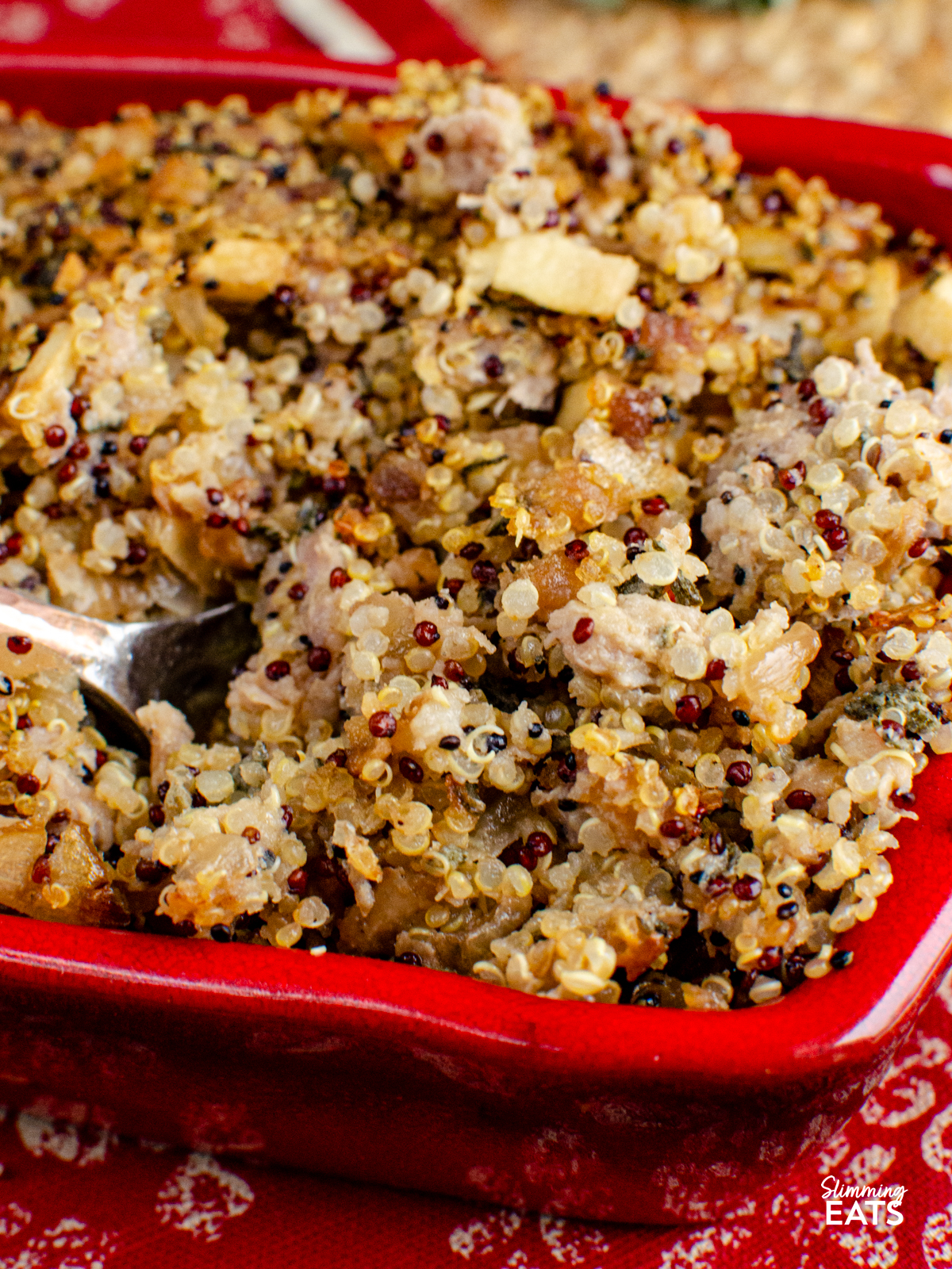 spoon scooping up Sausage Sage Onion Quinoa Stuffing from a red ceramic dish on a red and beige mat