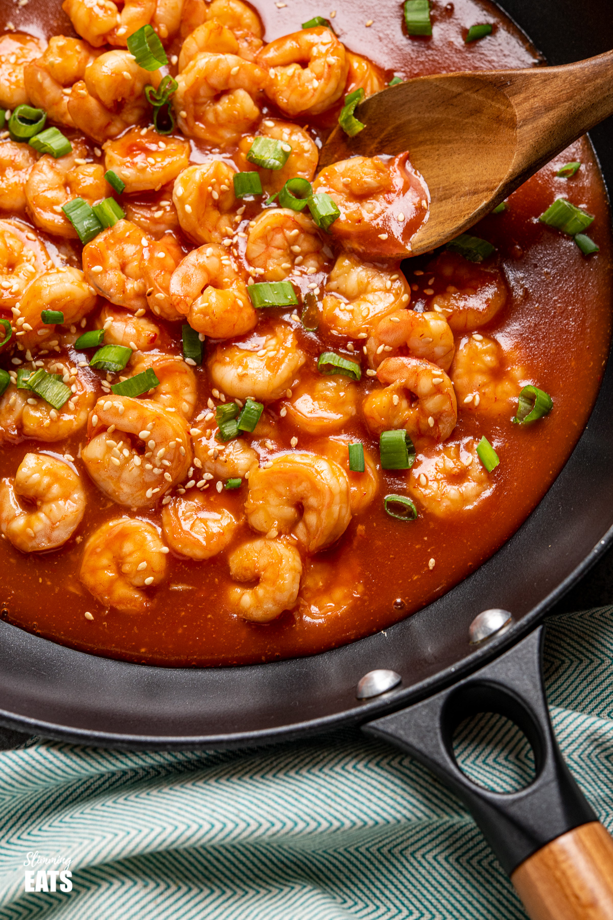 close up sweet and sour shrimp in black frying pan with wooden spoon