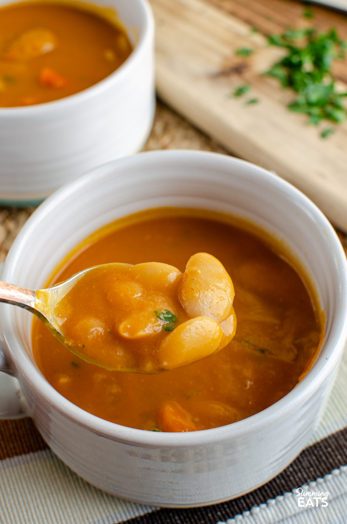 Carrot and Butter Bean Soup - a simple comforting soup with sweet carrots and creamy butter beans blended into a smooth flavour packed bowl that is perfect for lunch or a light dinner. It is quick to make, filling and delicious served with some warm crusty bread on the side. spooning up Carrot and Butter Bean Soup from a white with turquoise bottom soup mug with spoon