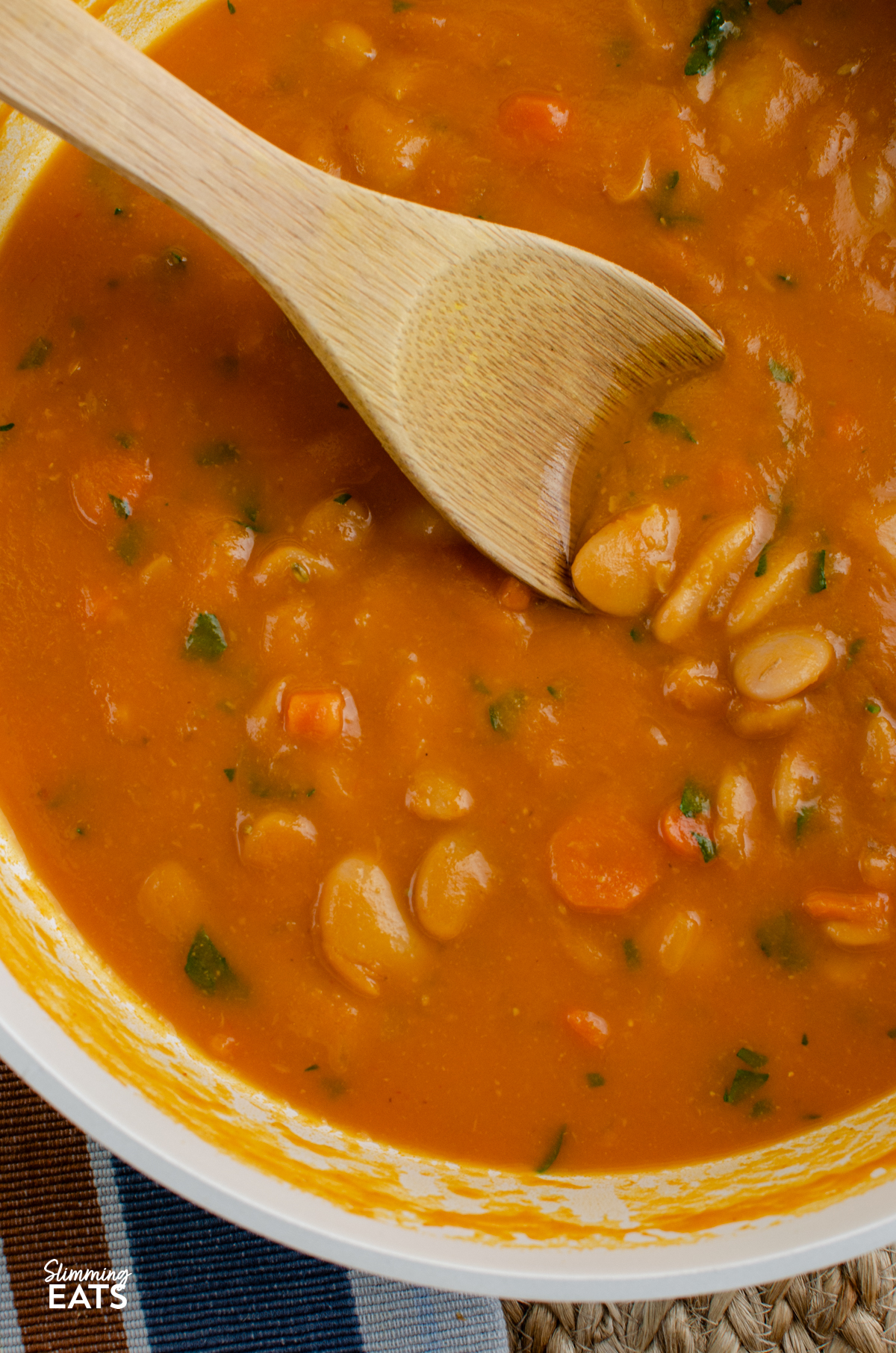 Carrot and Butter Bean Soup - a simple comforting soup with sweet carrots and creamy butter beans blended into a smooth flavour packed bowl that is perfect for lunch or a light dinner. It is quick to make, filling and delicious served with some warm crusty bread on the side. close up of Carrot and Butter Bean Soup in a double wooden handled ceramic non stick pan with wooden spoon