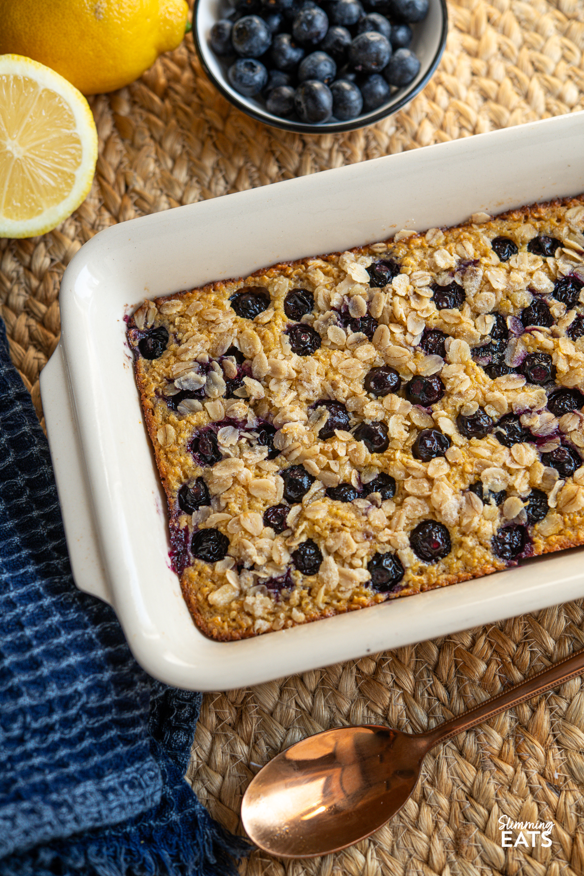 Freshly baked Lemon Blueberry Oats  in a baking dish, surrounded by a bowl of vibrant blueberrie, and slices of zesty lemon in the background.