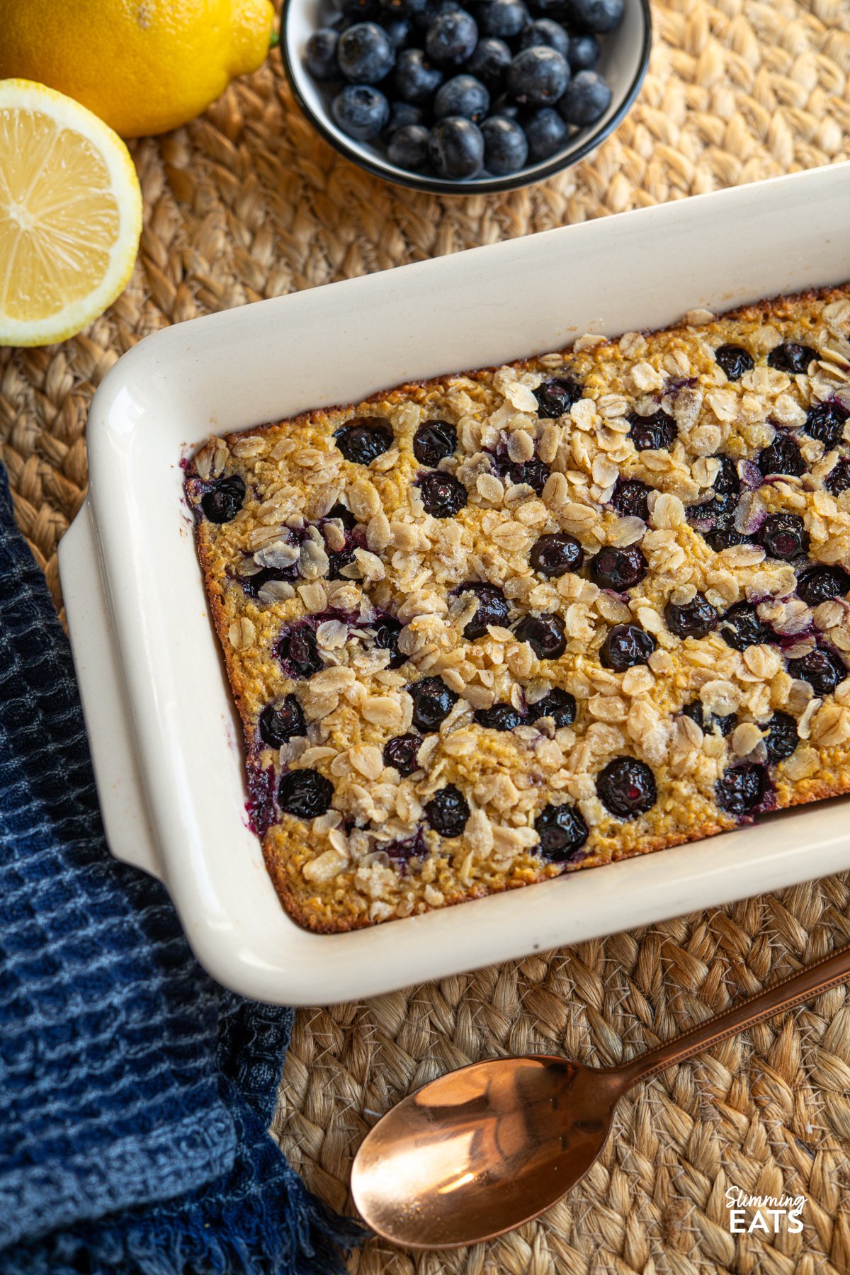 Enjoy the delightful blend of tangy lemon and sweet blueberries with Lemon and Blueberry Baked Oats. This recipe offers a perfect start to your day, combining the zesty freshness of lemon with the juiciness of blueberries for a nutritious and satisfying breakfast. Freshly baked Lemon Blueberry Oats in a baking dish, surrounded by a bowl of vibrant blueberrie, and slices of zesty lemon in the background.