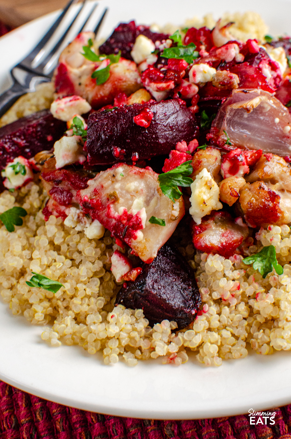 close up of serving of Chicken, Feta and Roasted Beetroot Bake on cooked quinoa on a white plate with a fork placed on left