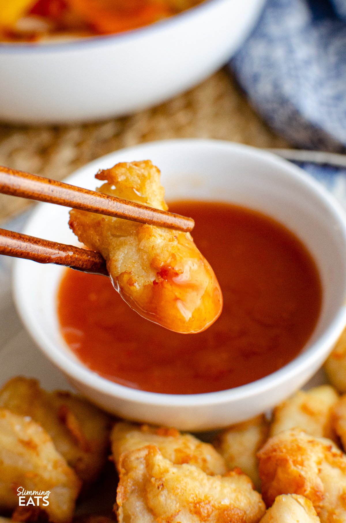 Forget takeout with this delicious Sweet and Sour Chicken Bites that can be cooked in an Air Fryer or Oven and are the perfect addition to your Chinese fakeaway night. chopsticks holding a sweet and sour chicken bite dipped in sweet and sour sauce