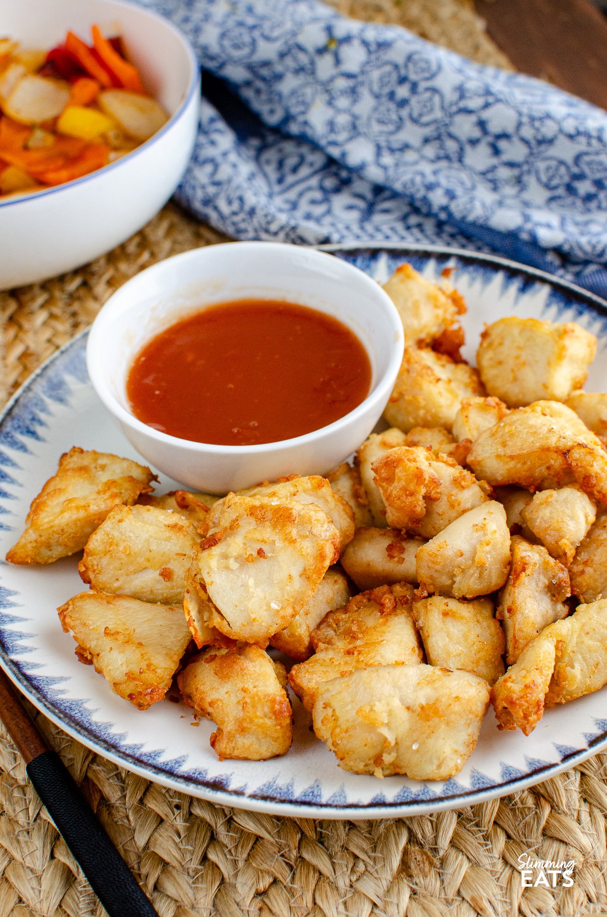 Forget takeout with this delicious Sweet and Sour Chicken Bites that can be cooked in an Air Fryer or Oven and are the perfect addition to your Chinese fakeaway night. sweet and sour chicken bites on a plate with a blue and navy patterned rim, small bowl of sweet and sour sauce on the side