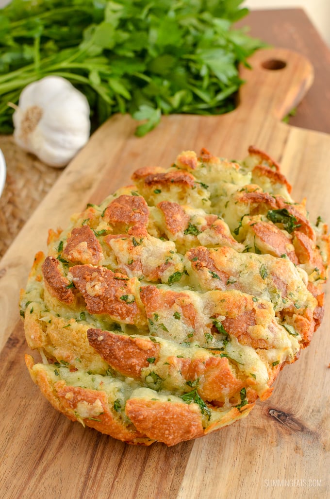 pull-apart cheesy garlic bread on wooden board with garlic and parsley