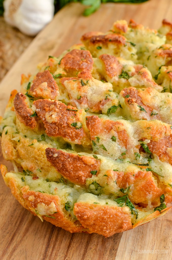 Pull-Apart Cheesy Garlic Oat Bread on wooden board with garlic and herbs in background