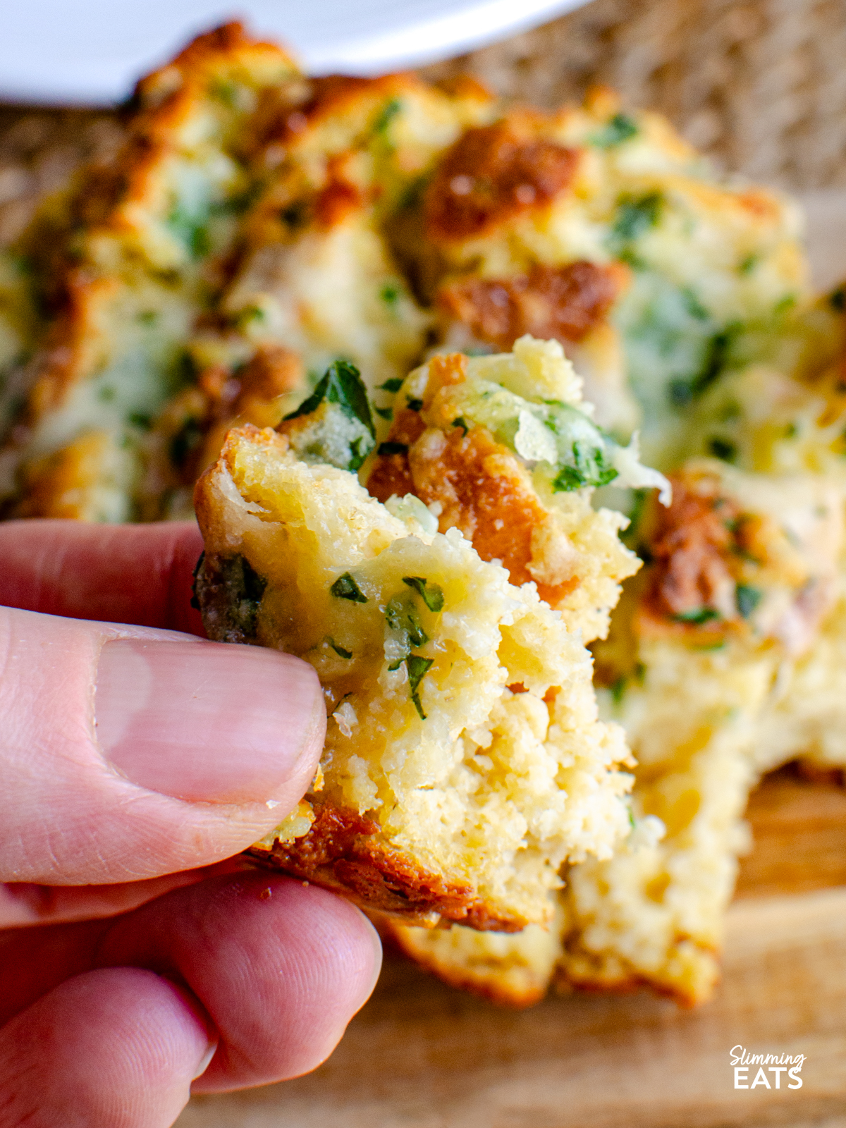 piece of out of oven cheesy oat garlic bread pulled from loaf on board.