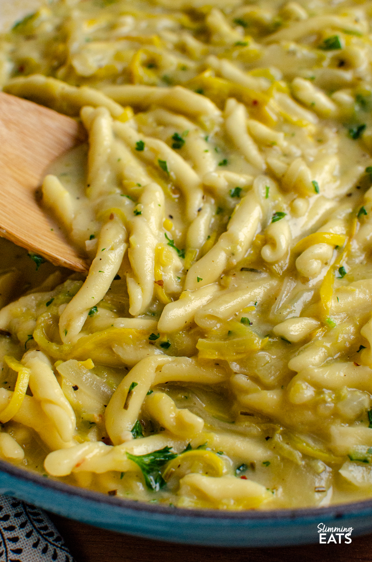 Dairy Free Yellow Zucchini Pasta - a creamy comforting one pot pasta dish made with simple ingredients and completely dairy free. Sweet yellow zucchini, garlic and pasta come together in a silky sauce, with light coconut milk adding that delicious creamy texture without needing any cheese or cream. close up of One Pot Dairy Free Creamy Yellow Zucchini Pasta in a blue ceramic cast iron skillet with wooden spoon
