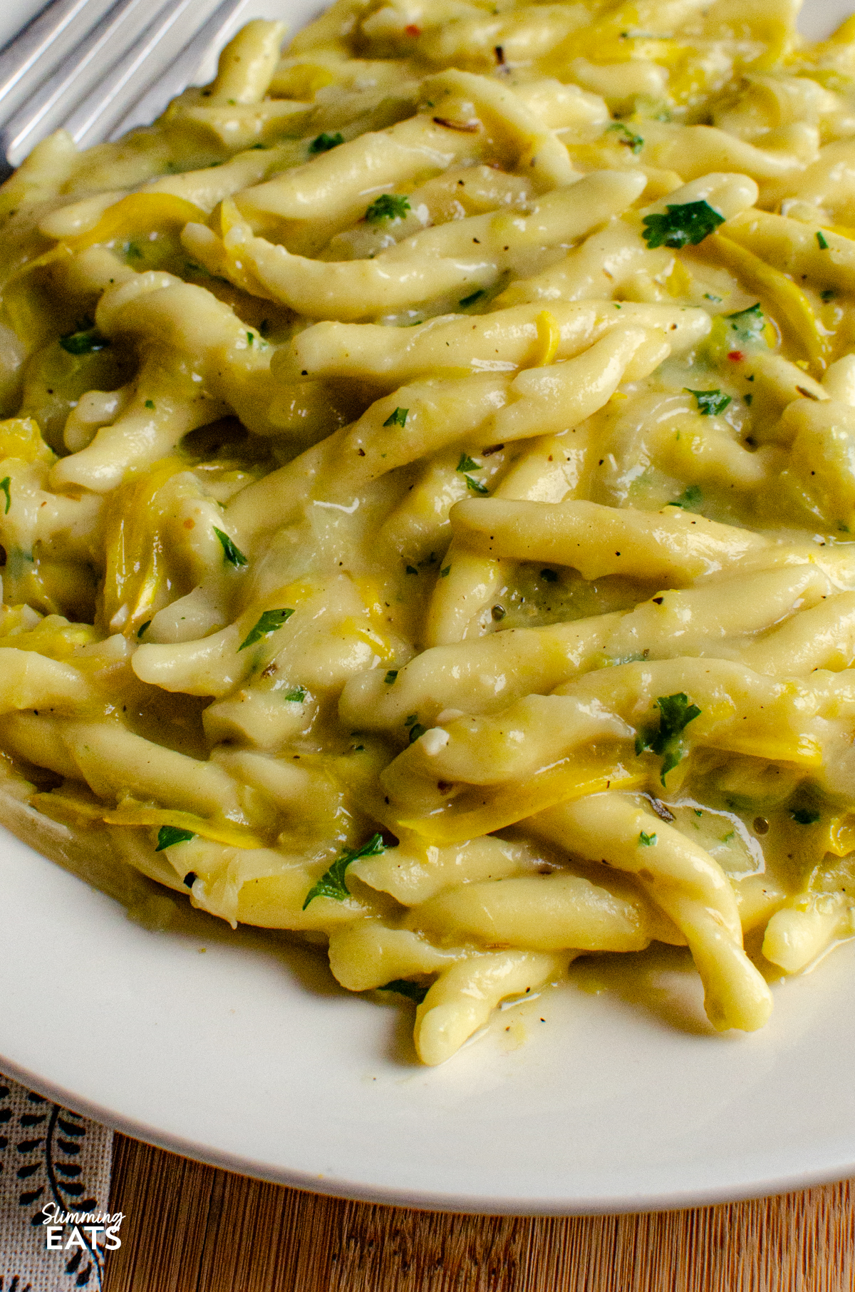 Dairy Free Yellow Zucchini Pasta - a creamy comforting one pot pasta dish made with simple ingredients and completely dairy free. Sweet yellow zucchini, garlic and pasta come together in a silky sauce, with light coconut milk adding that delicious creamy texture without needing any cheese or cream. close up of serving of One Pot Dairy Free Creamy Yellow Zucchini Pasta on a white plate with a fork