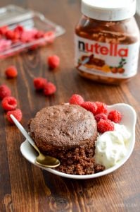 gluten free microwave chocolate cake in a mug with raspberries and cream with spoon and Nutella