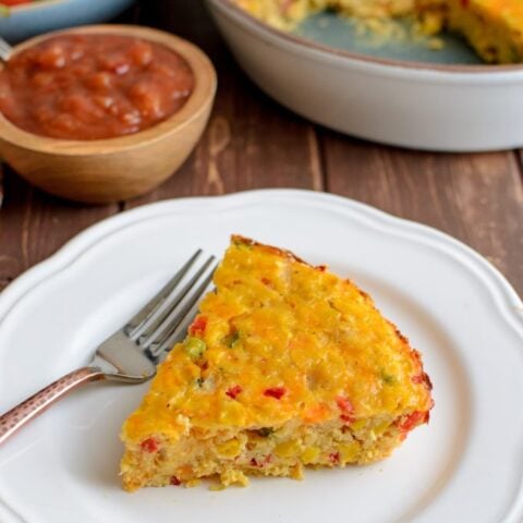 slice of lentil cheddar sweetcorn bake on plate with salad and salsa