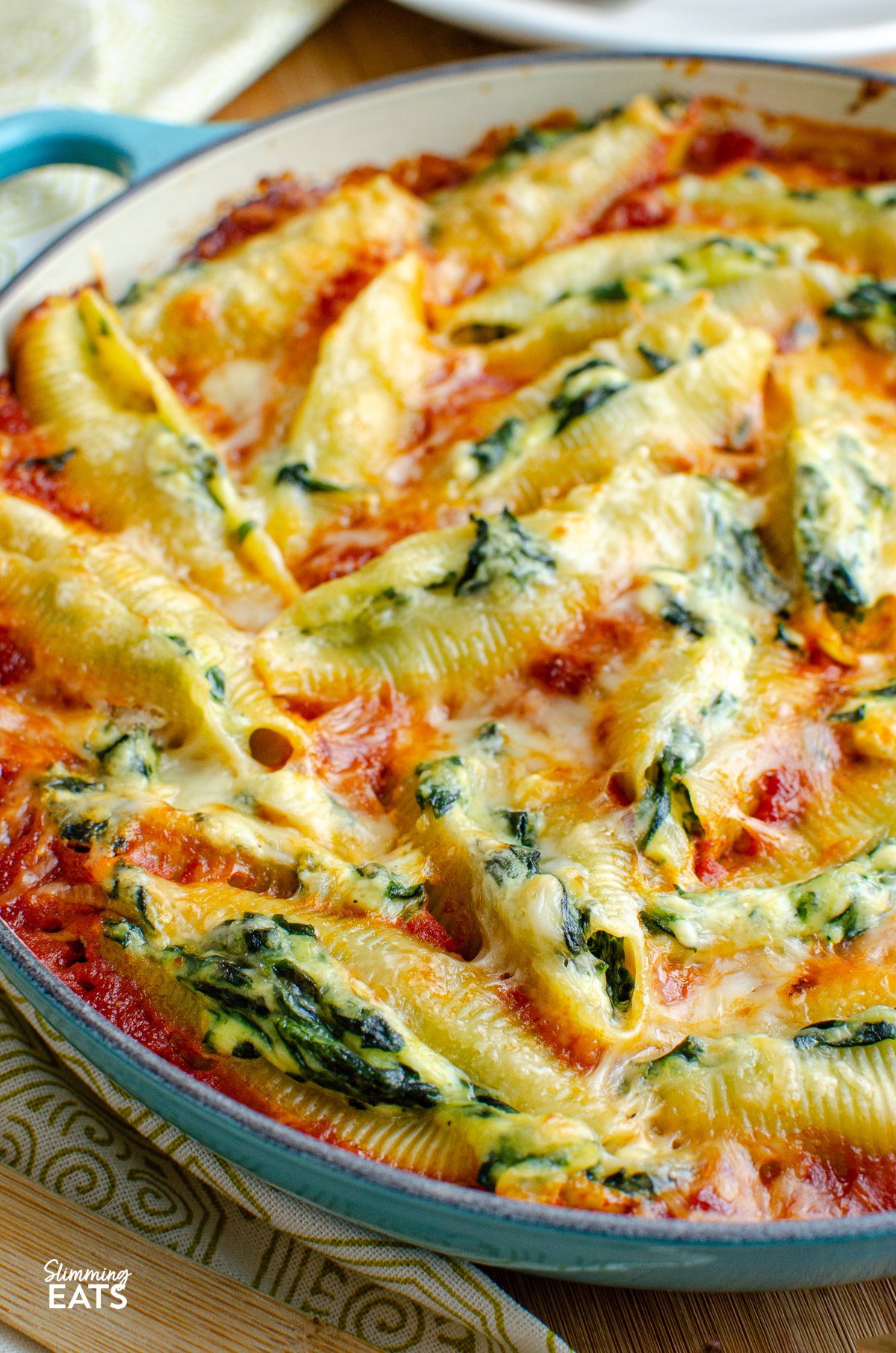 Ricotta and Spinach Stuffed Pasta Shells presented in a turquoise cast iron pan, accompanied by a wooden spoon.