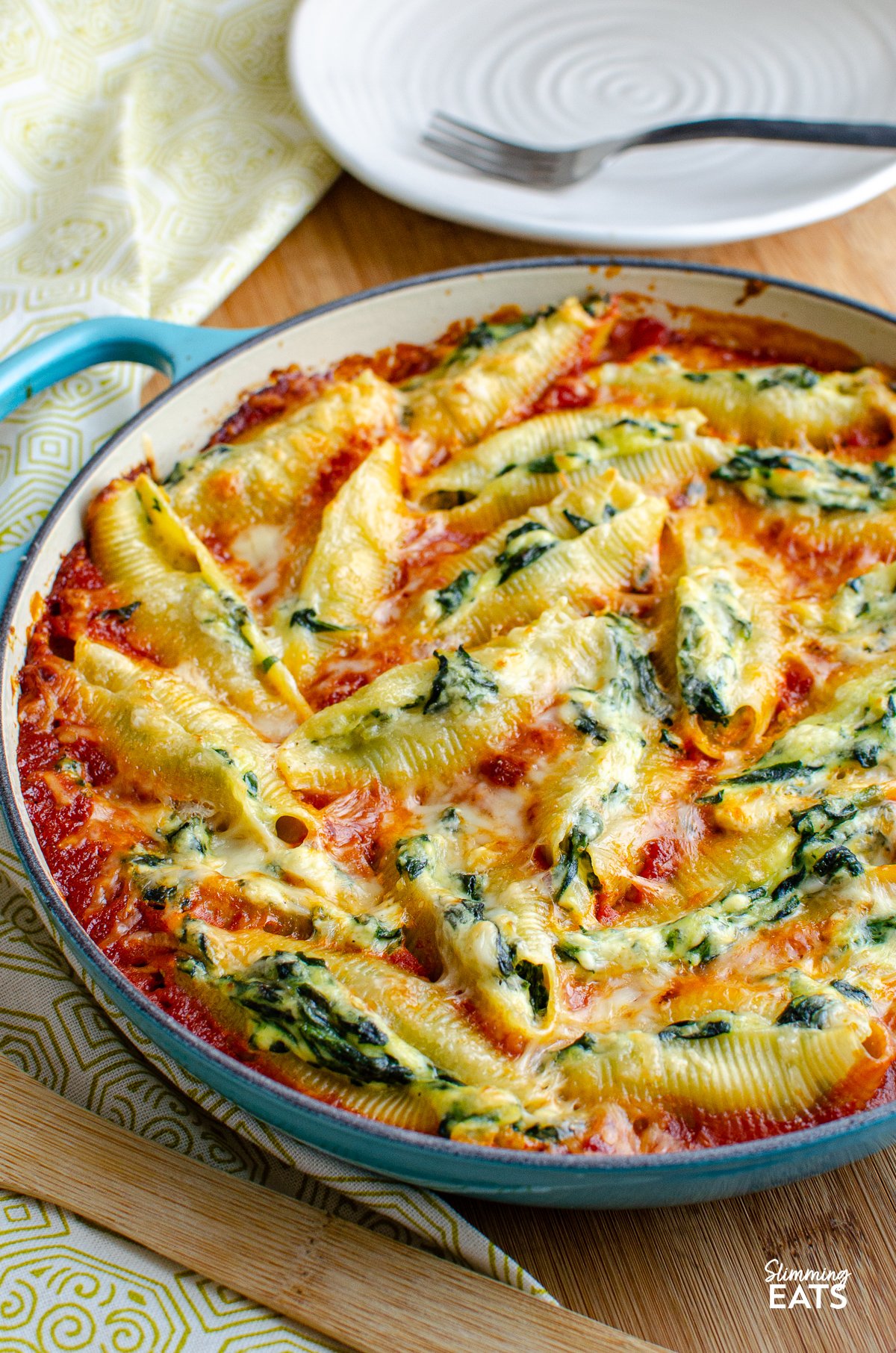 Ricotta and Spinach Stuffed Pasta Shells presented in a turquoise cast iron pan, accompanied by a wooden spoon.