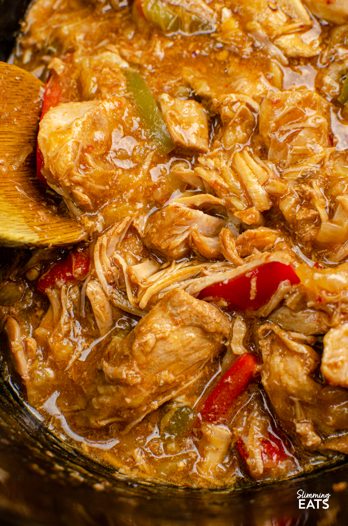 Slow Cooker Pineapple Pork - tender slow cooked pork in a delicious sweet and savoury sauce with pineapple, peppers, soy sauce and a little kick of spice. It is the perfect easy dinner that is ideal for busy days when you want dinner ready and waiting for you when you get home. close up of Pineapple Pork in slow cooker with wooden spoon