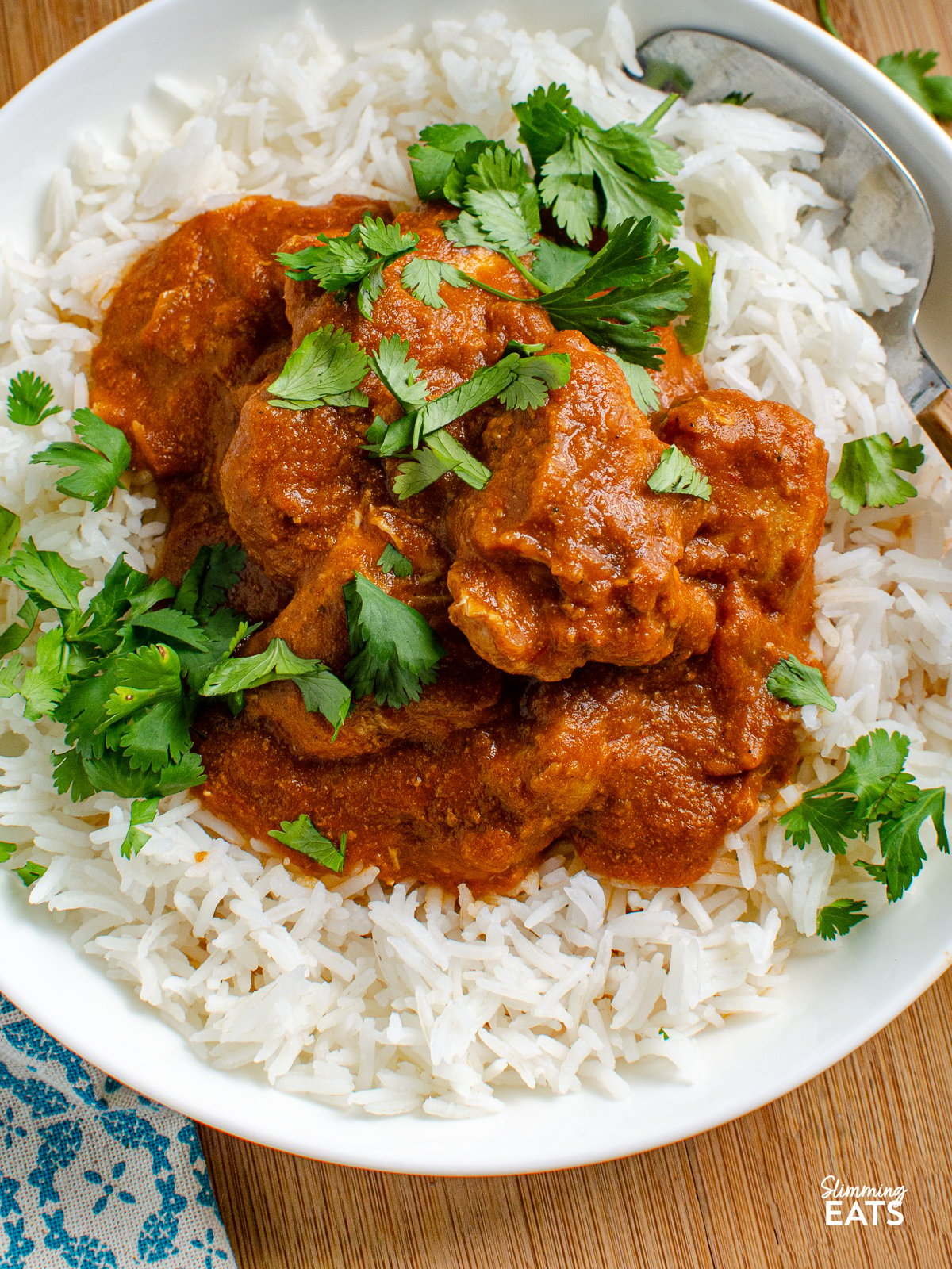 close up of serving of butter chicken in bowl with white ric and sprinkled with coriander