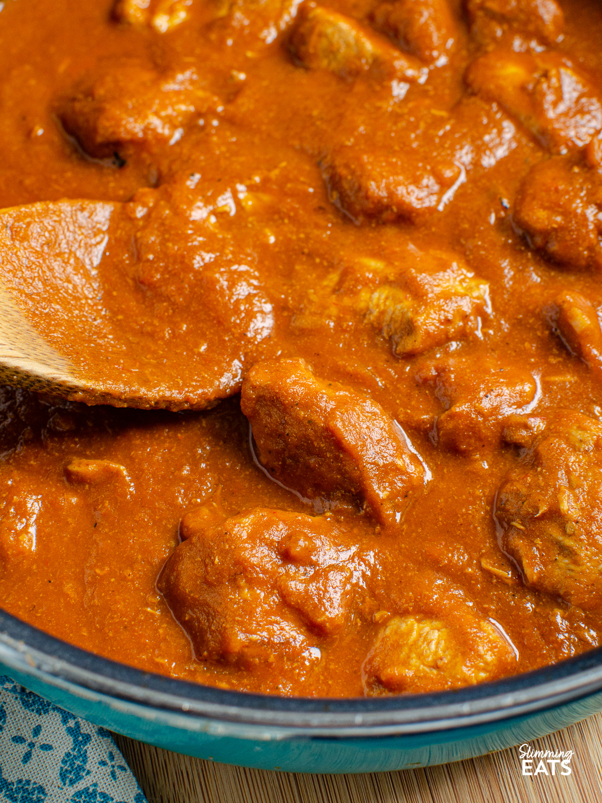close up of butter chicken in pan with wooden spoon