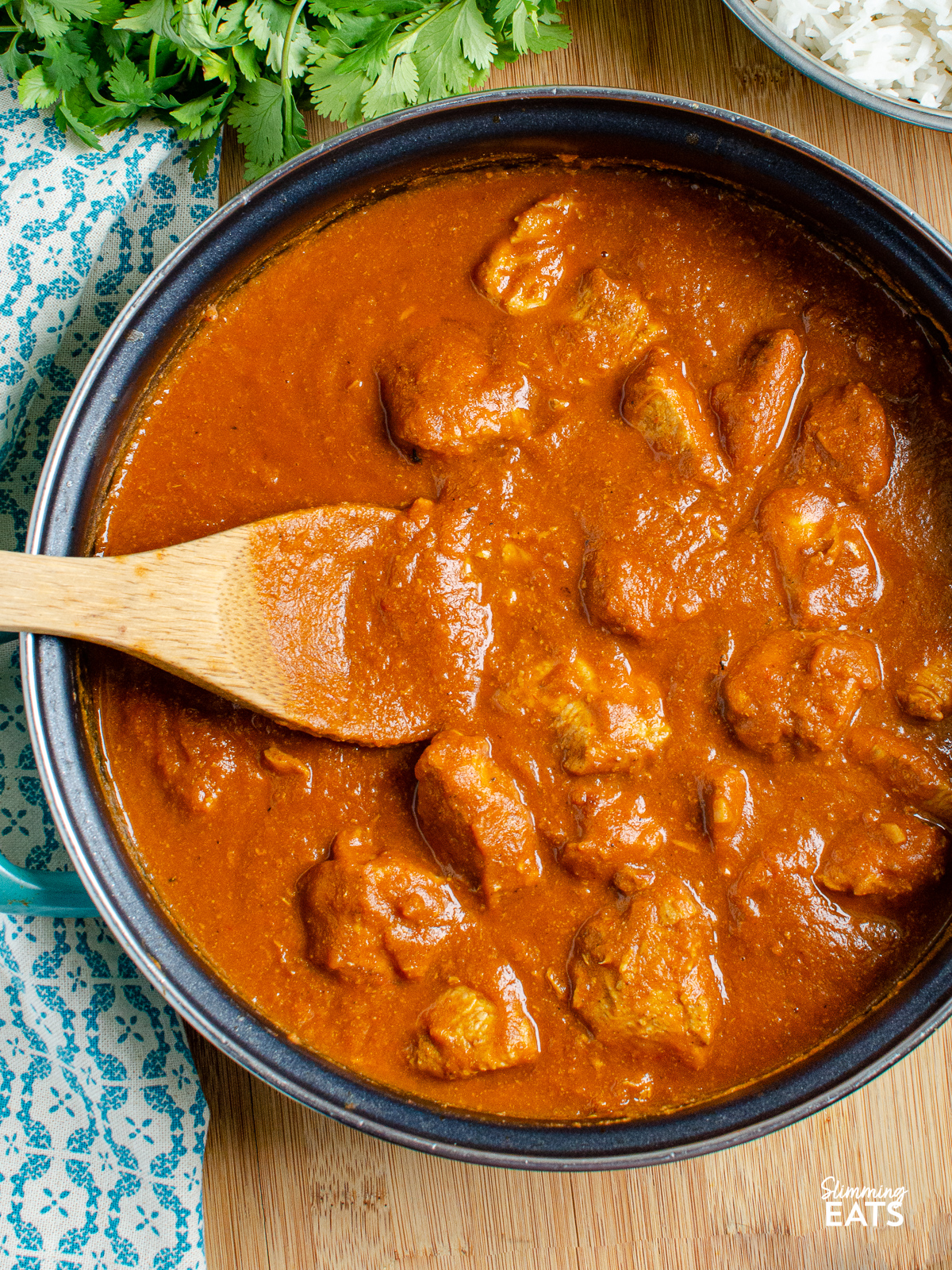 over top view of butter chicken in frying pan with wooden spoon 