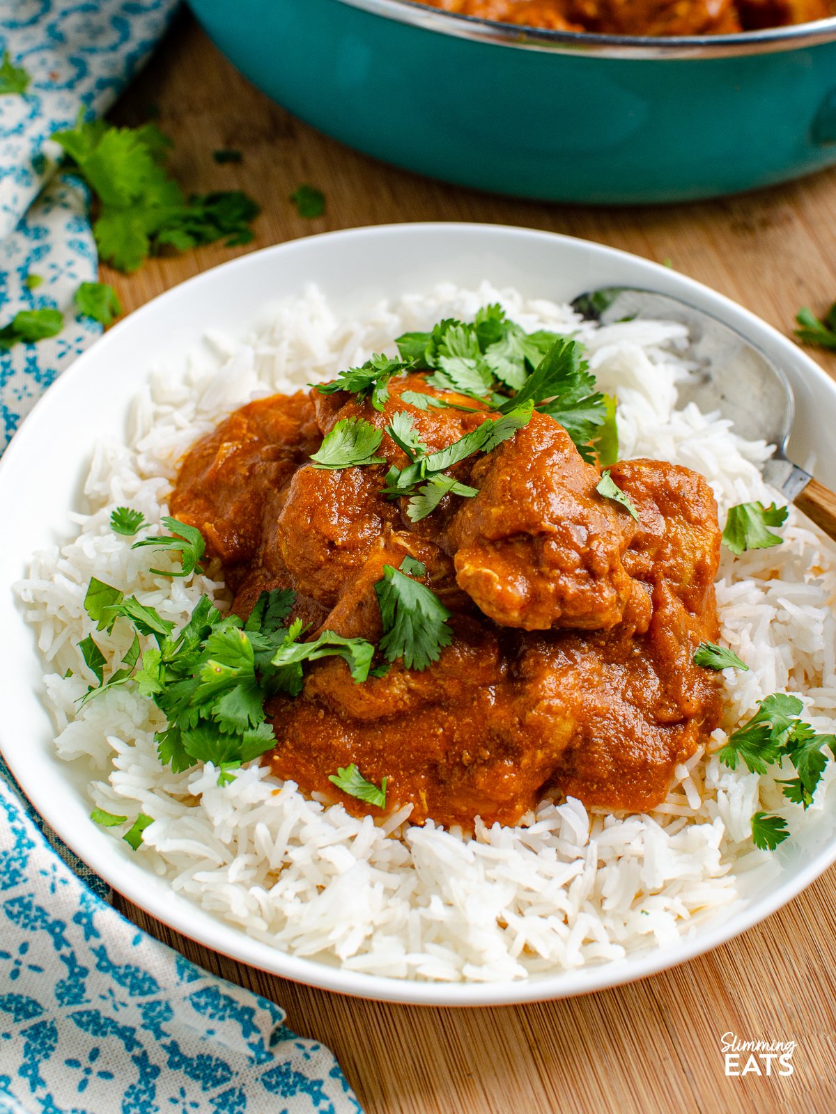 serving of butter chicken with rice in a white bowl sprinkled with coriander