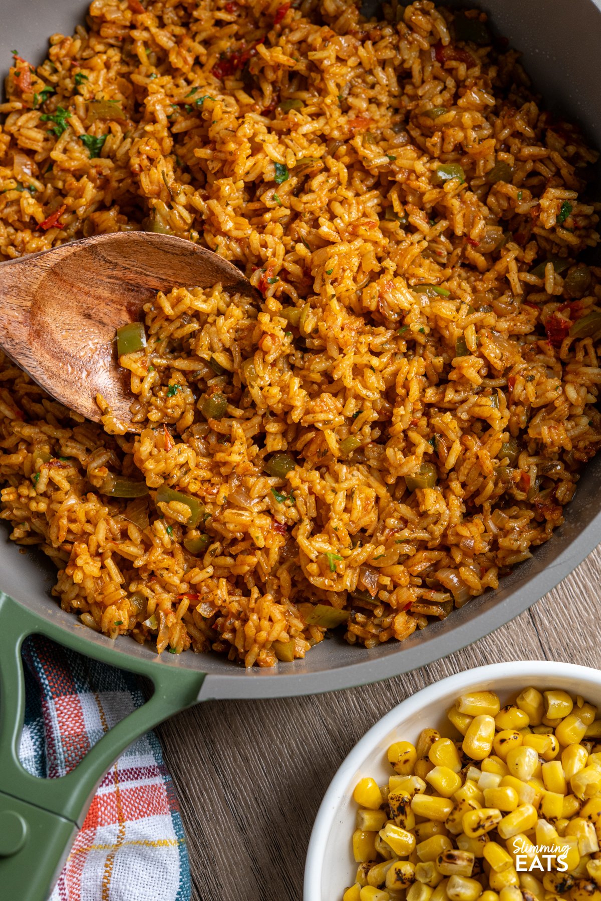 If you’re anything like me, a Nando’s fakeaway night isn’t complete without that iconic spicy rice on the side. This One Pot Nando’s-Style Peri Peri Rice brings all those bold, fiery flavours into your kitchen with simple, fresh ingredients and absolutely no fuss. It’s inspired by the much-loved restaurant favourite, but made at home with pantry staples and a good pinch of love. The best part? It’s all cooked in one pot, so you get maximum flavour without a mountain of washing up. close up of nandos style peri peri rice in our place green non stick frying pan with wooden spoon, next to a bowl of charred corn