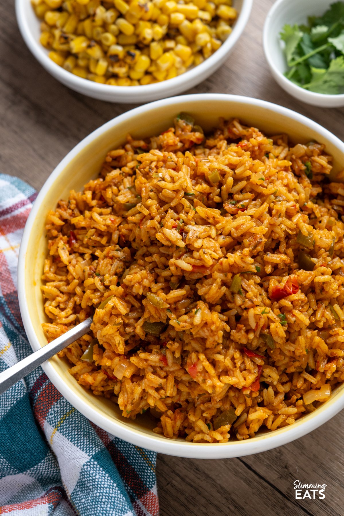 If you’re anything like me, a Nando’s fakeaway night isn’t complete without that iconic spicy rice on the side. This One Pot Nando’s-Style Peri Peri Rice brings all those bold, fiery flavours into your kitchen with simple, fresh ingredients and absolutely no fuss. It’s inspired by the much-loved restaurant favourite, but made at home with pantry staples and a good pinch of love. The best part? It’s all cooked in one pot, so you get maximum flavour without a mountain of washing up. close up of nandos style peri peri rice in white and yellow bowl next to small bowls of charred corn and cilantro.