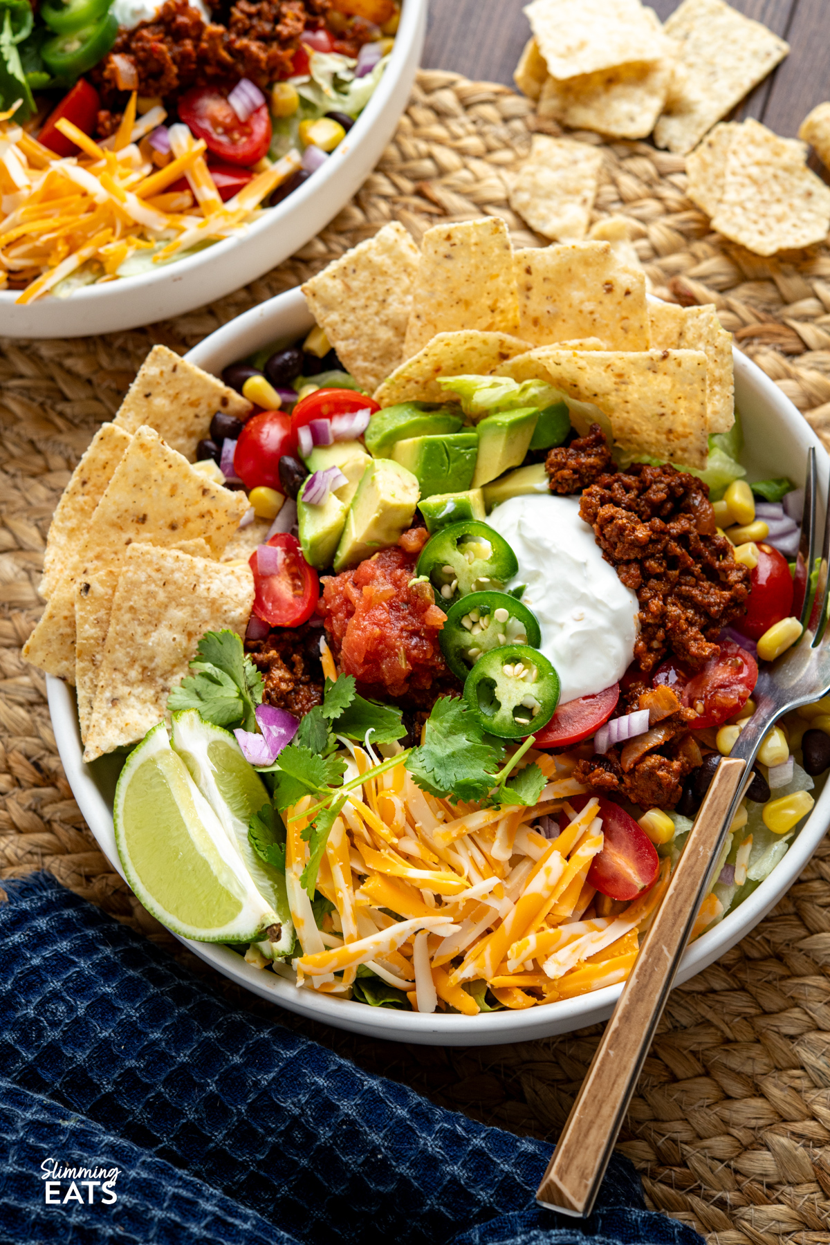 These Taco Salad Bowls are packed with all the delicious flavours of tacos, served over a fresh, colourful salad for an easy meal that is hearty, satisfying and perfect for lunch or dinner. plated up taco salad bowl with beans, corn, avocado, salsa, soured cream, onion, lettuce, tortilla chips, cheddar and jalapenos.