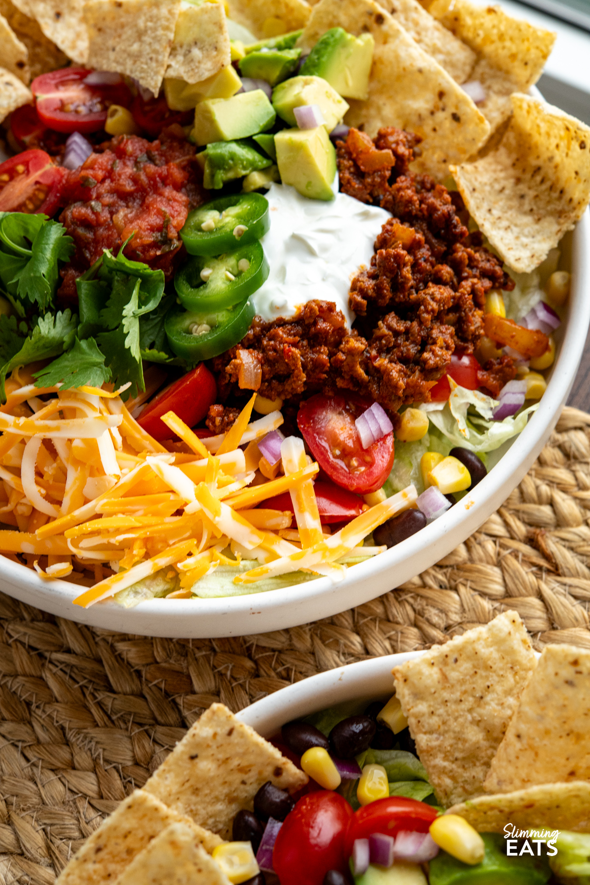 These Taco Salad Bowls are packed with all the delicious flavours of tacos, served over a fresh, colourful salad for an easy meal that is hearty, satisfying and perfect for lunch or dinner. close up of plated up taco salad bowl with beans, corn, avocado, salsa, soured cream, onion, lettuce, tortilla chips, cheddar and jalapenos.