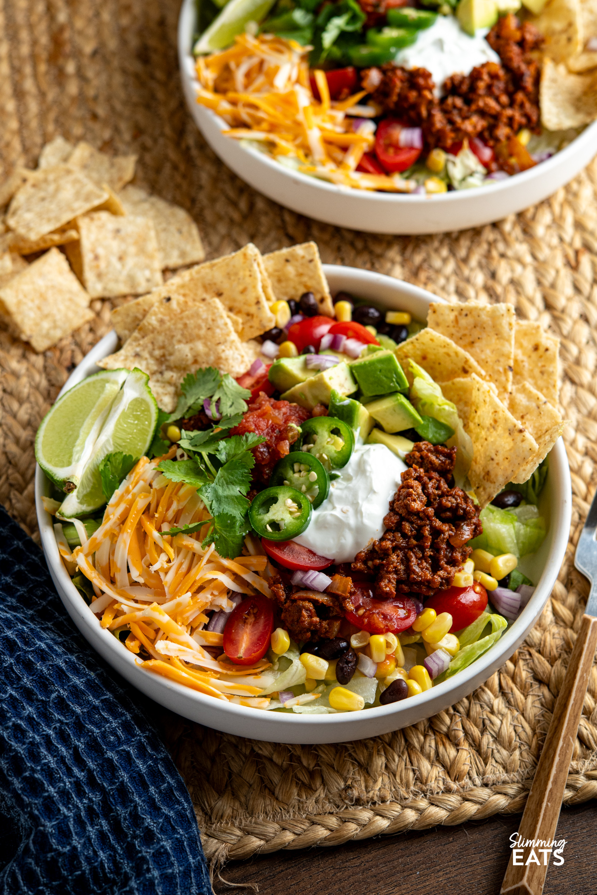 These Taco Salad Bowls are packed with all the delicious flavours of tacos, served over a fresh, colourful salad for an easy meal that is hearty, satisfying and perfect for lunch or dinner. plated up taco salad bowl with beans, corn, avocado, salsa, soured cream, onion, lettuce, tortilla chips, cheddar and jalapenos.