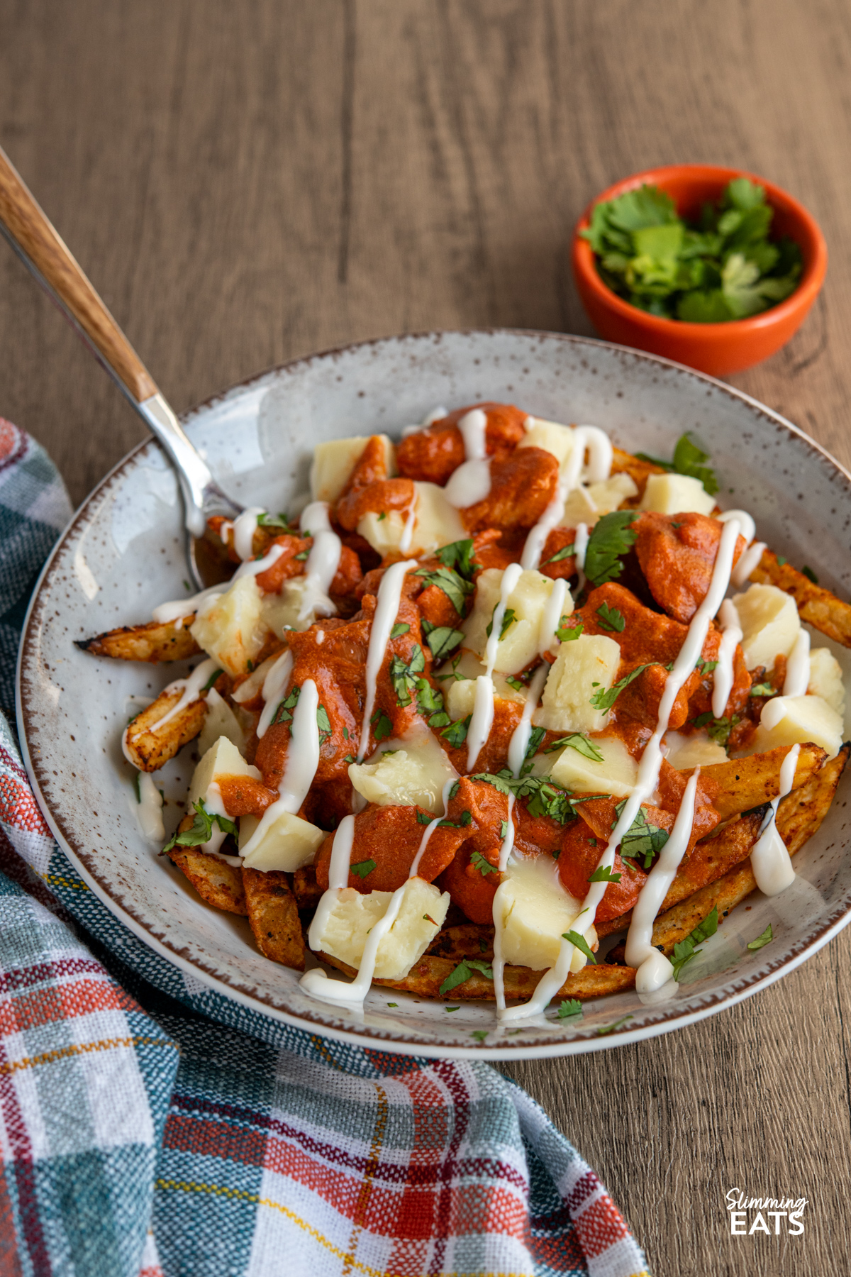Butter Chicken Poutine!! - The ultimate dish for leftover butter chicken with crispy fries, melty cheese and plenty of flavour. Butter Chicken Poutine in a brown grey bowl with fork, small orange bowl of coriander next to bowl.
