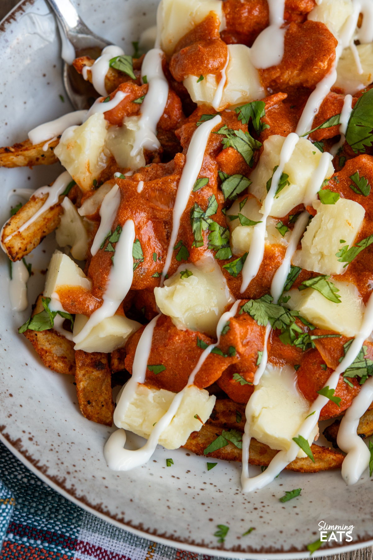Butter Chicken Poutine!! - The ultimate dish for leftover butter chicken with crispy fries, melty cheese and plenty of flavour. close up of Butter Chicken Poutine in a brown grey bowl with fork