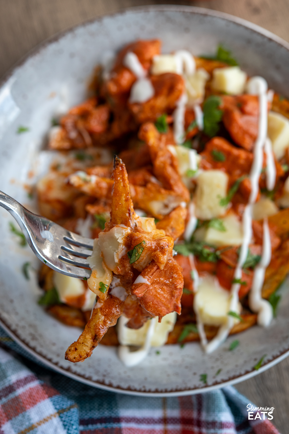 Butter Chicken Poutine!! - The ultimate dish for leftover butter chicken with crispy fries, melty cheese and plenty of flavour. fork picking up Butter Chicken Poutine from a brown grey bowl