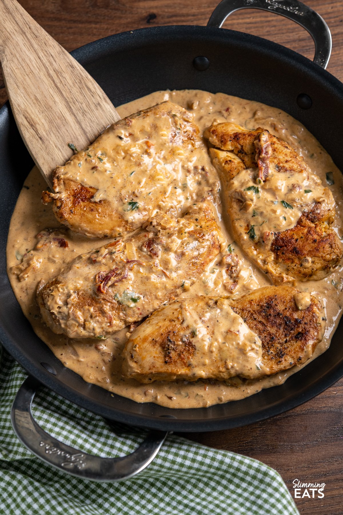 Chicken in Creamy Sun-dried Tomato Sauce - This mouthwatering dish features tender and juicy chicken breasts smothered in a rich and tangy sauce made with low-fat cream cheese and sun-dried tomatoes. close up of Chicken in Creamy Sun-dried Tomato Sauce in black frying pan with wooden spatula