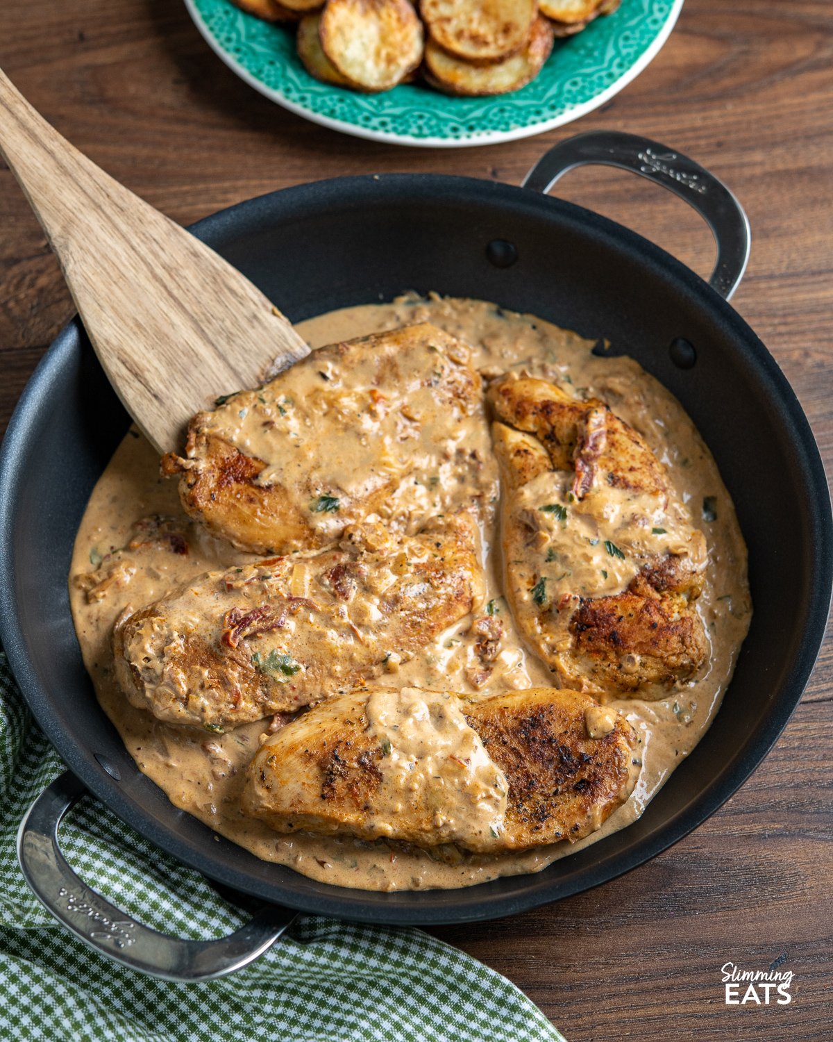 Chicken in Creamy Sun-dried Tomato  Sauce in black double handled frying pan with wooden spatula