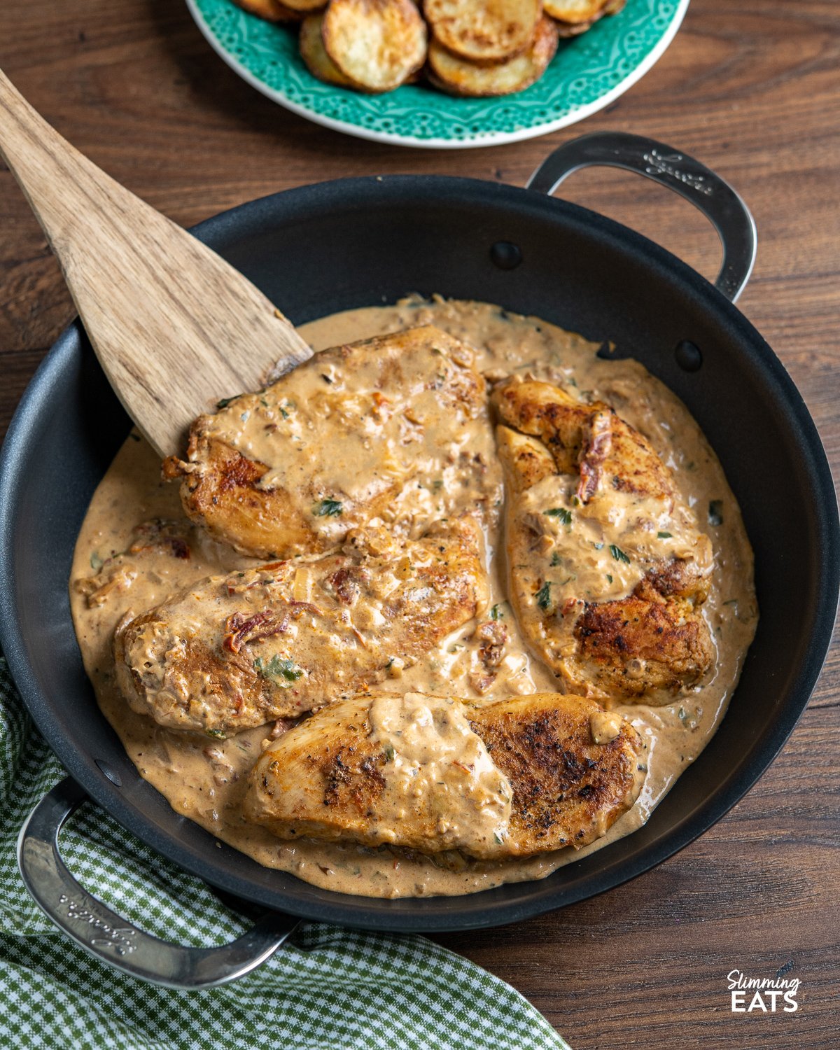 Chicken in Creamy Sun-dried Tomato Sauce - This mouthwatering dish features tender and juicy chicken breasts smothered in a rich and tangy sauce made with low-fat cream cheese and sun-dried tomatoes. Chicken in Creamy Sun-dried Tomato Sauce in black double handled frying pan with wooden spatula