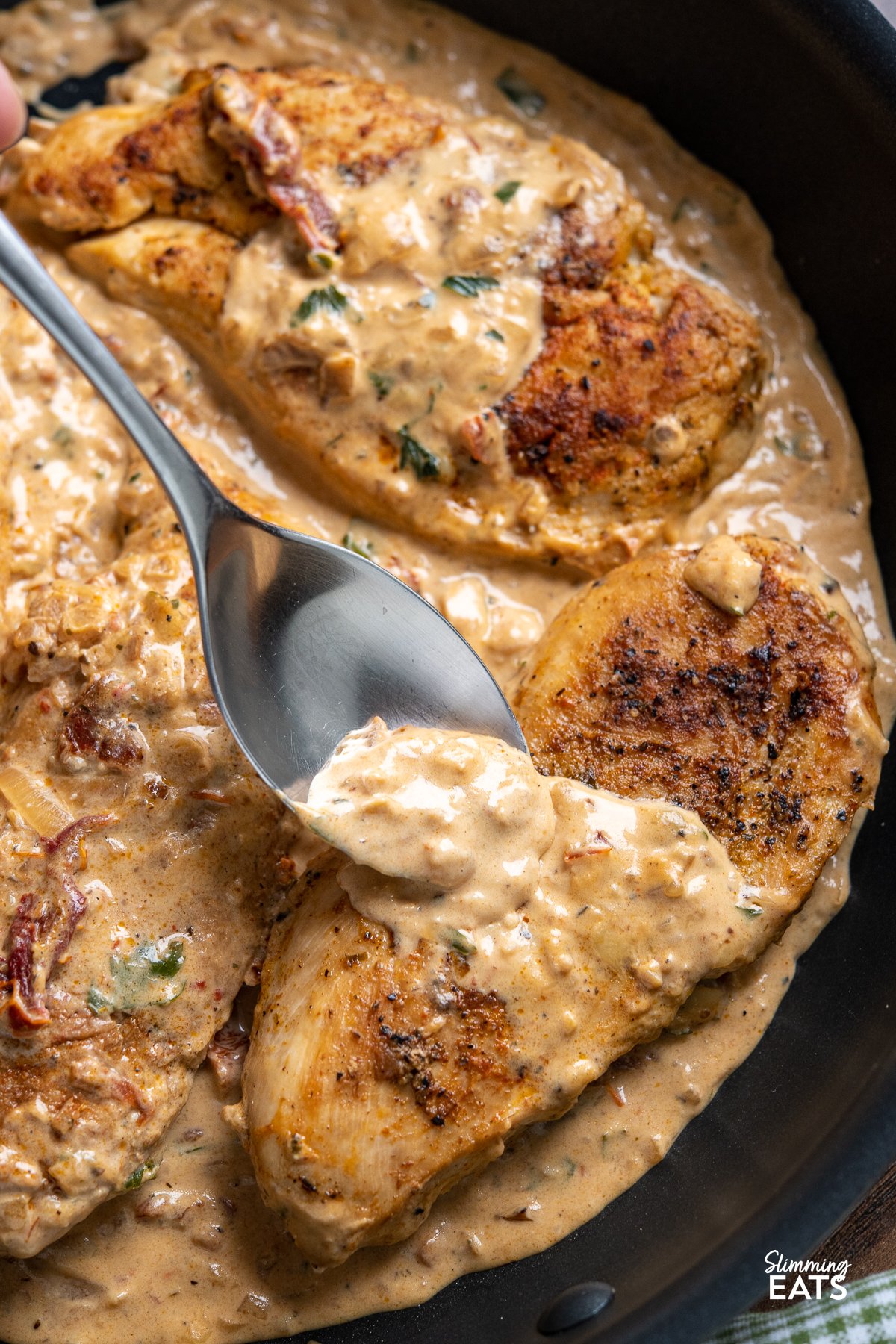 Chicken in Creamy Sun-dried Tomato Sauce - This mouthwatering dish features tender and juicy chicken breasts smothered in a rich and tangy sauce made with low-fat cream cheese and sun-dried tomatoes. spoon spooning Creamy Sun-dried Tomato Sauce over chicken breast