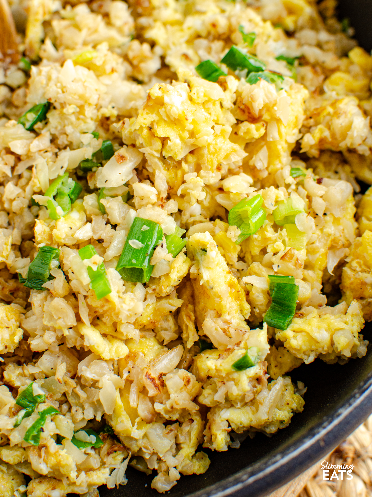 close up of egg fried cauliflower rice in wooden handled skillet