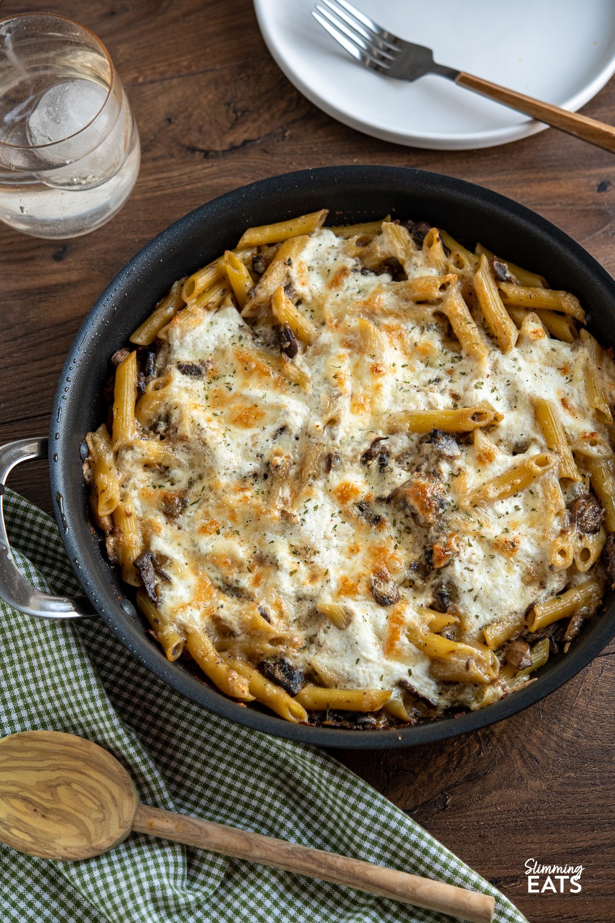 Baked Garlic Mushroom and Ricotta Pasta in a frying pan with wooden spoon and green white chequed napkin