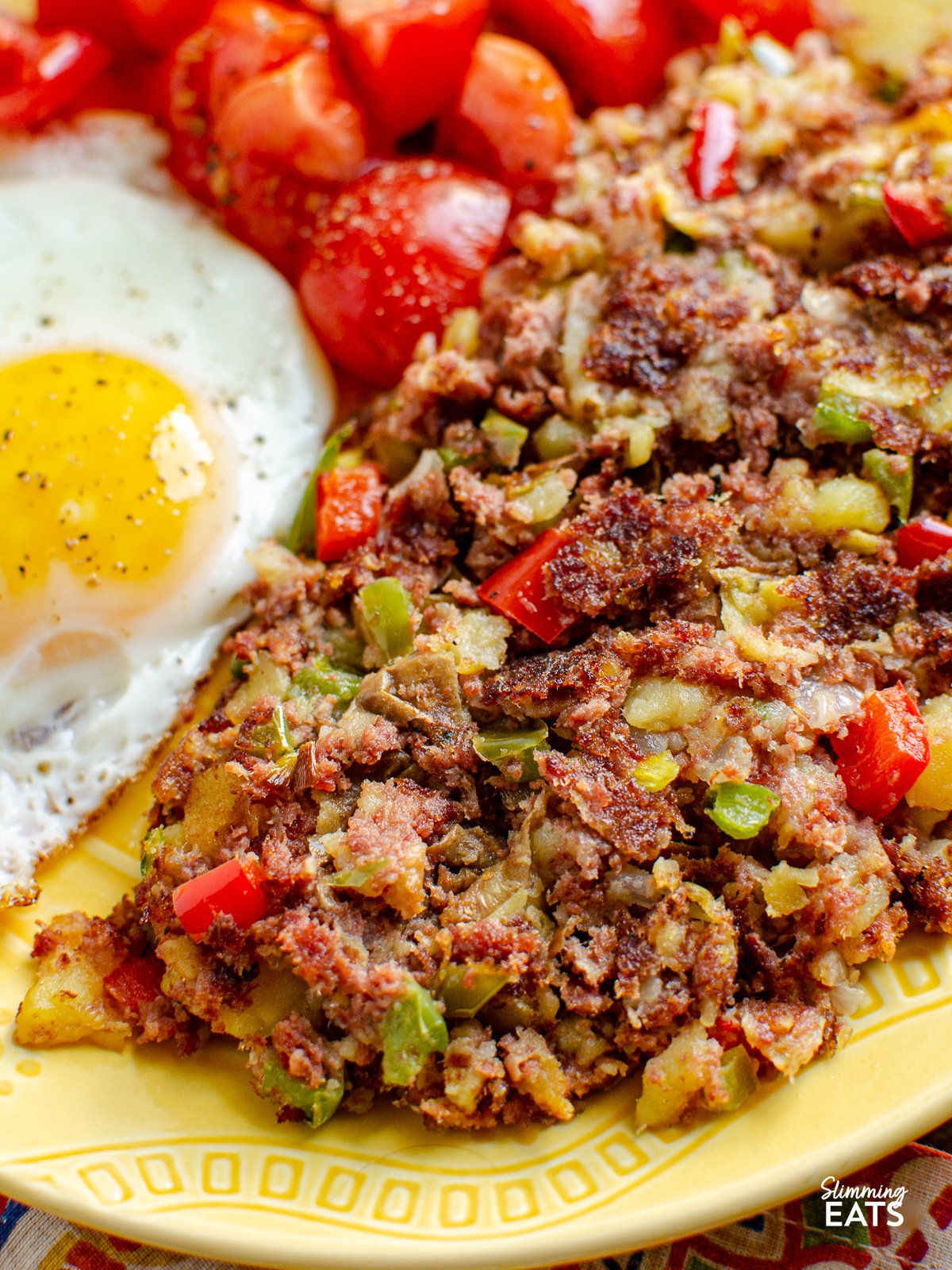 close up of Corned Beef Hash  on a yellow plate with fried egg and ripe grape tomatoes