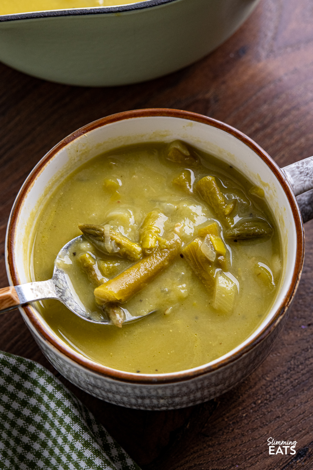 Asparagus Soup in a brown and white soup cup with a spoon placed in cup
