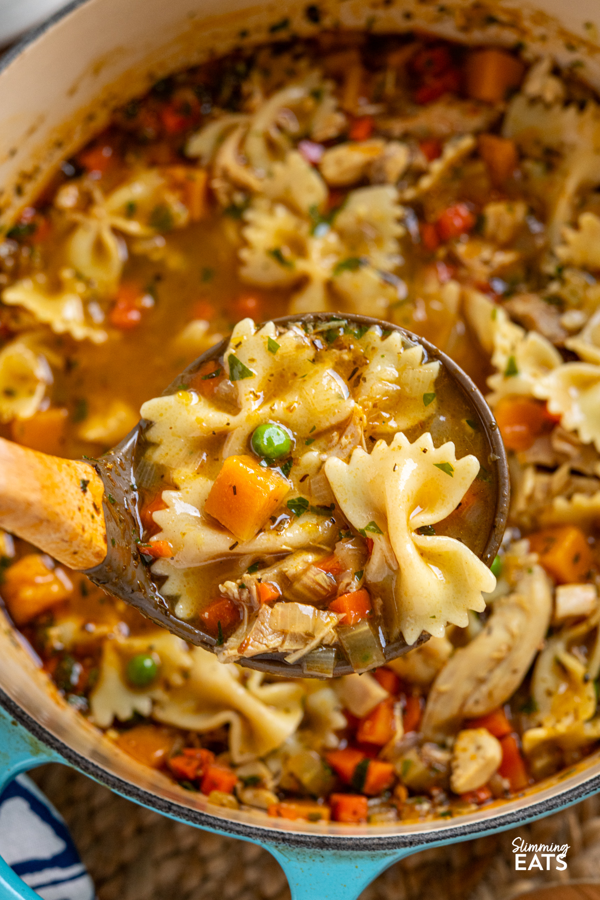 ladle spooning up chicken vegetable pasta soup from turquoise cast iron enameled pot 