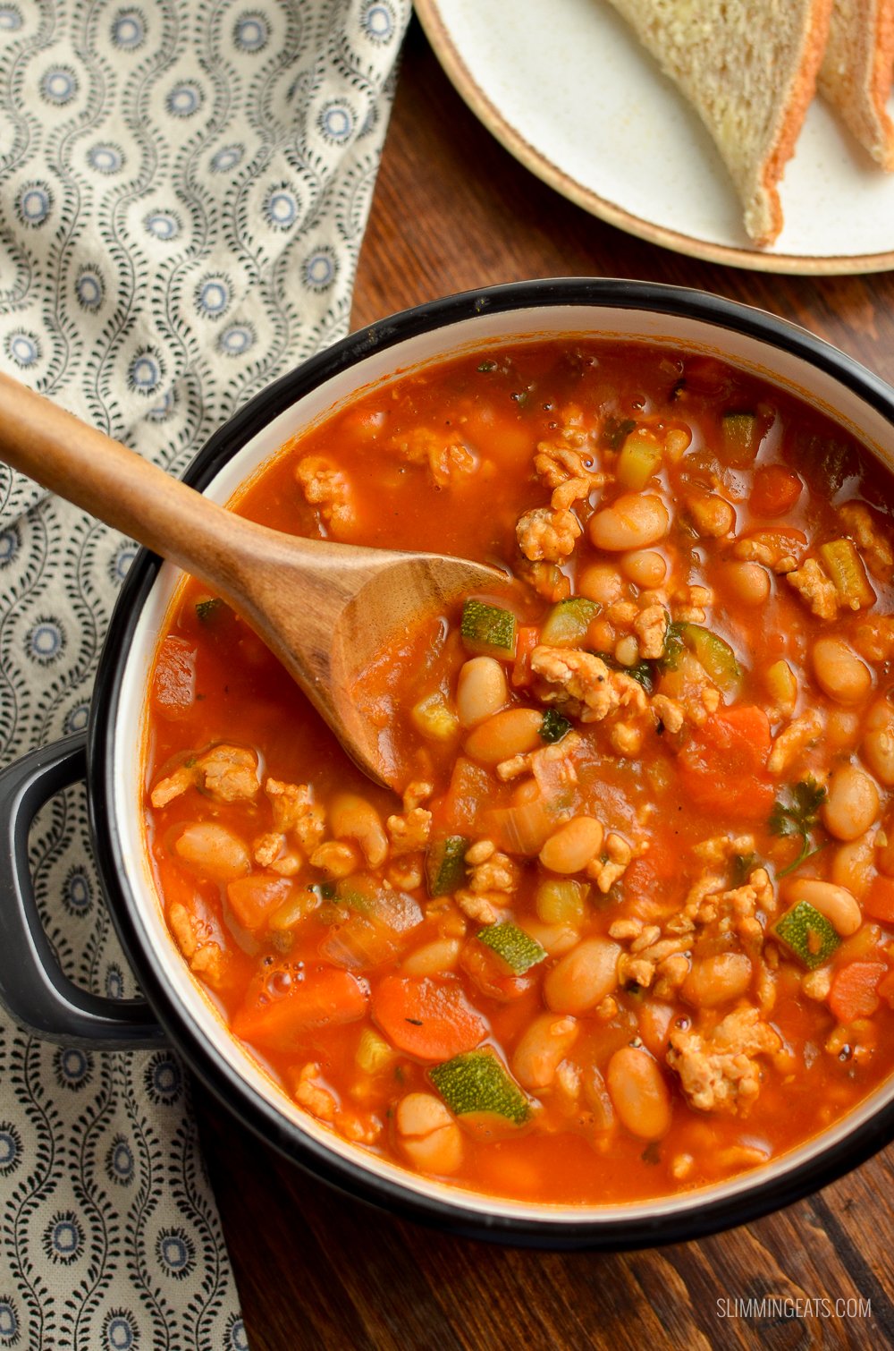 saucepan of ground turkey vegetable bean soup with wooden spoon and bread and butter in background