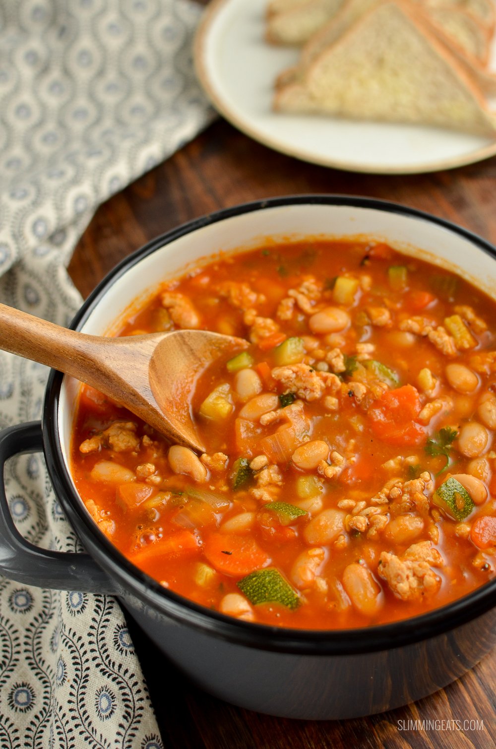 grey saucepan of ground turkey vegetable bean soup with bread and butter on plate