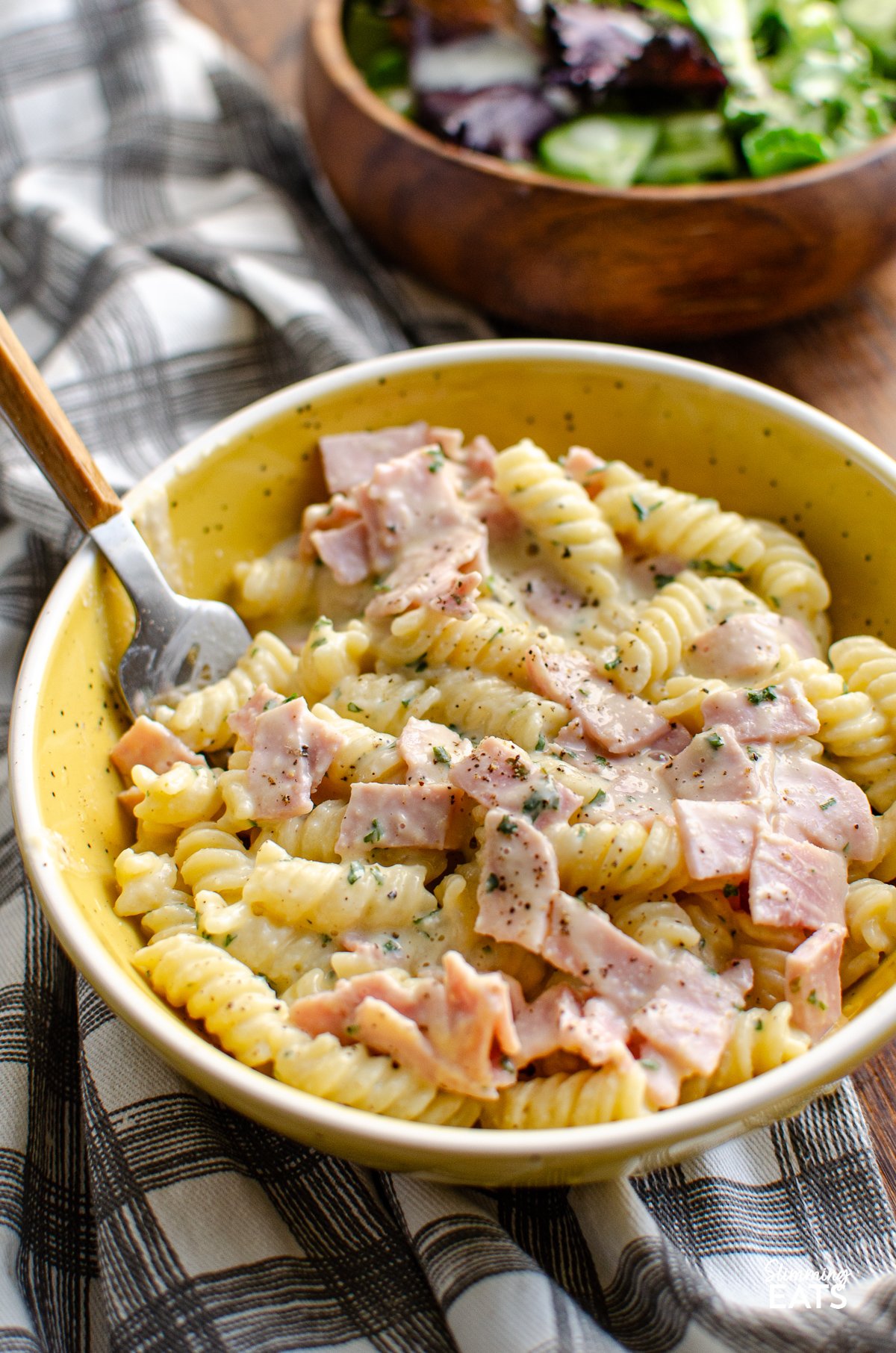  Quick Creamy Pasta in white and yellow bowl with fork and wooden bowl in background with baby greens