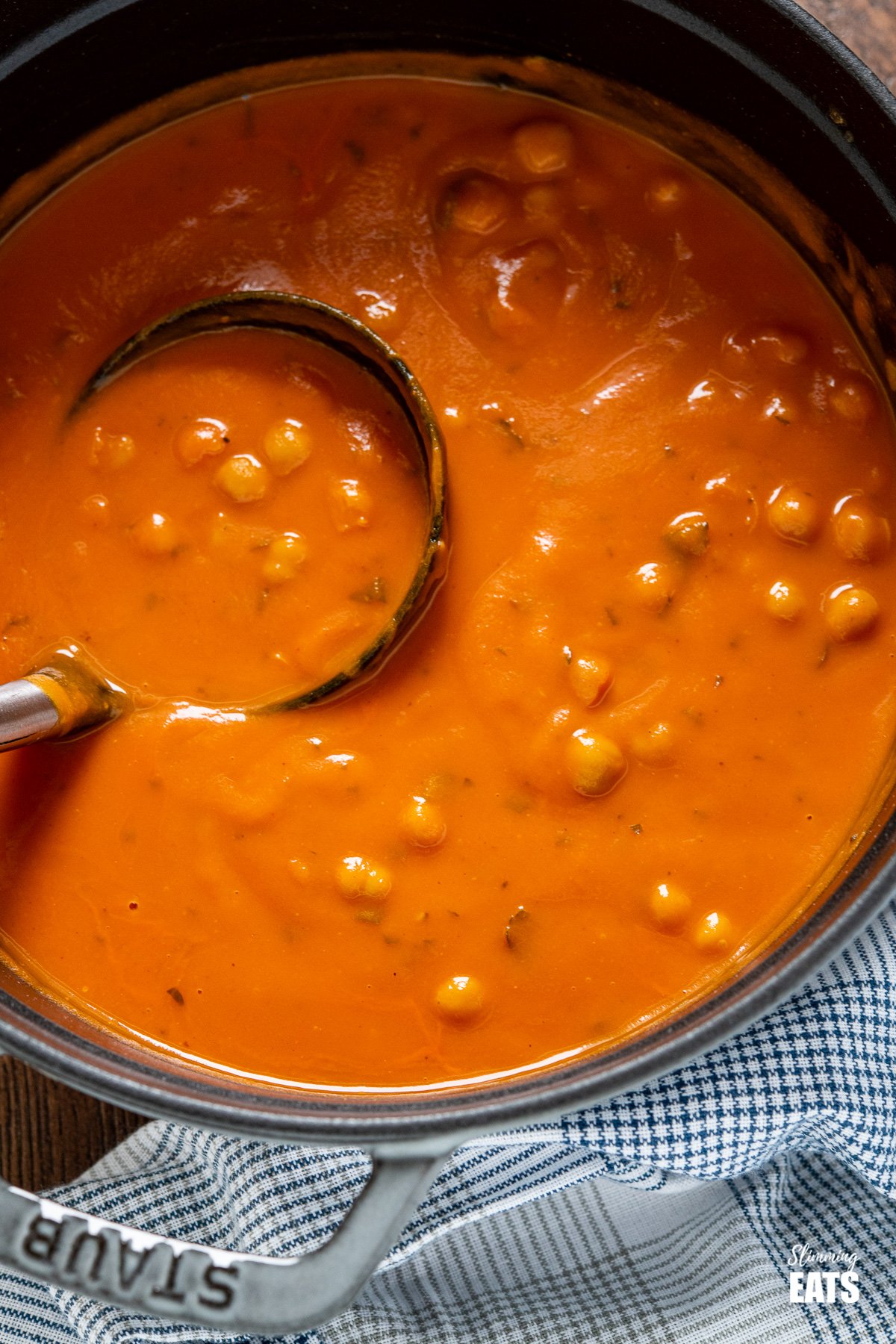 close up of soup spoon in Chickpea and Tomato Soup in grey staub cast iron pan.