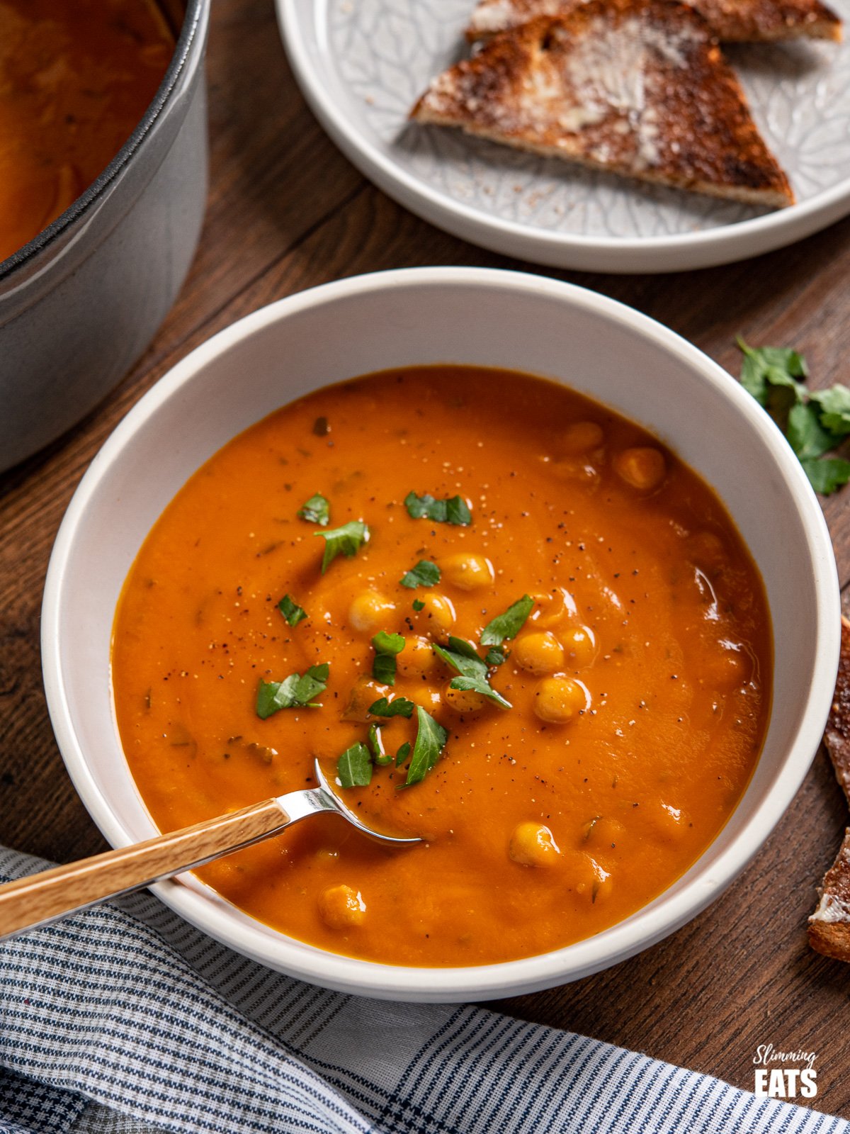 chickpeas and tomato soup in grey bowl with spoon and scattered parsley
